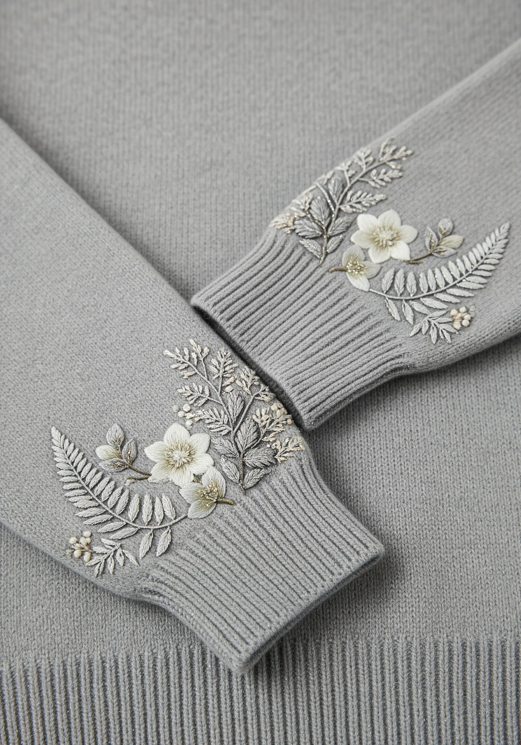 Delicate white and green floral embroidery on the ribbed cuff of a grey sweater