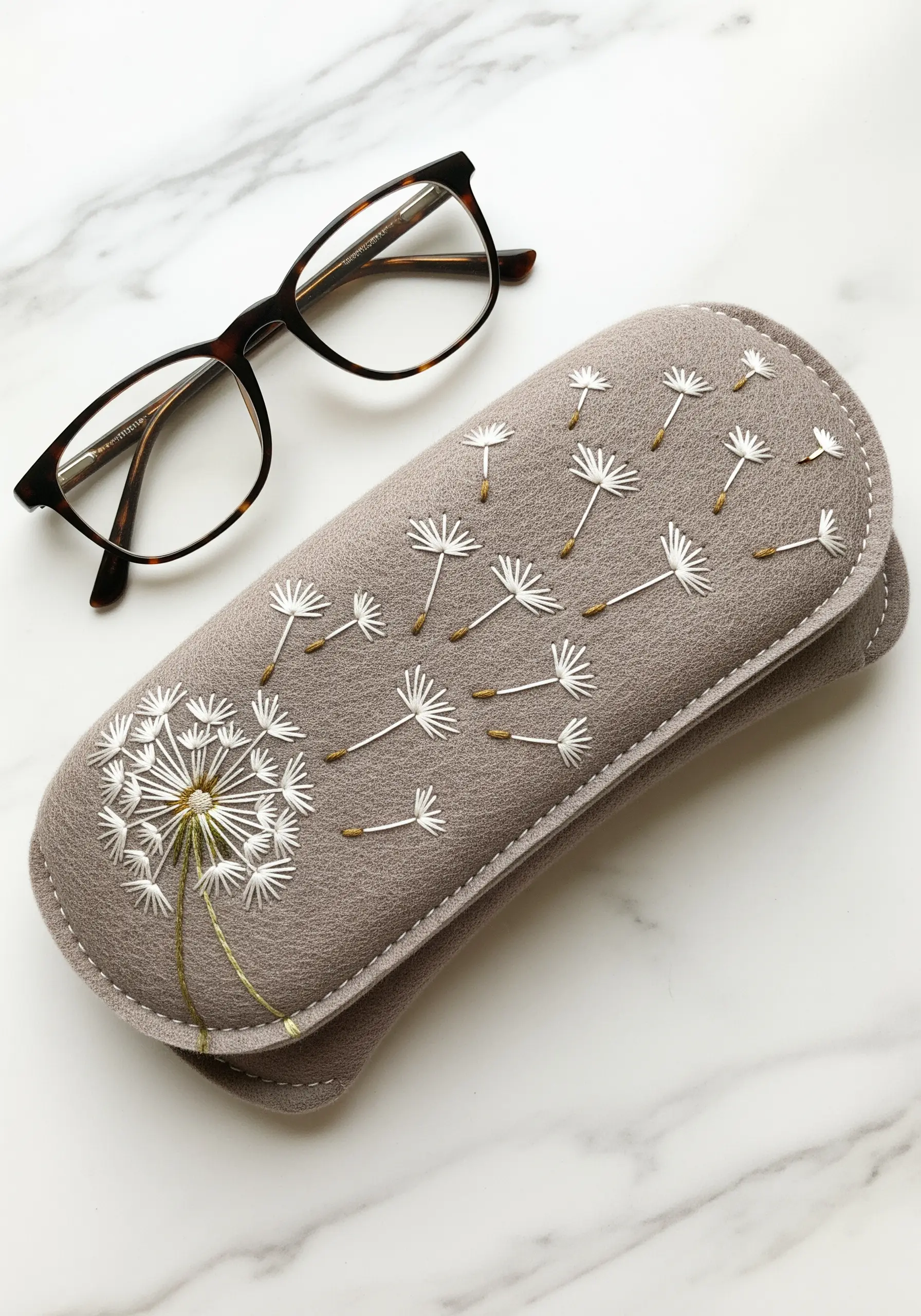 A dandelion with seeds blowing in the wind, embroidered on a gray felt glasses case