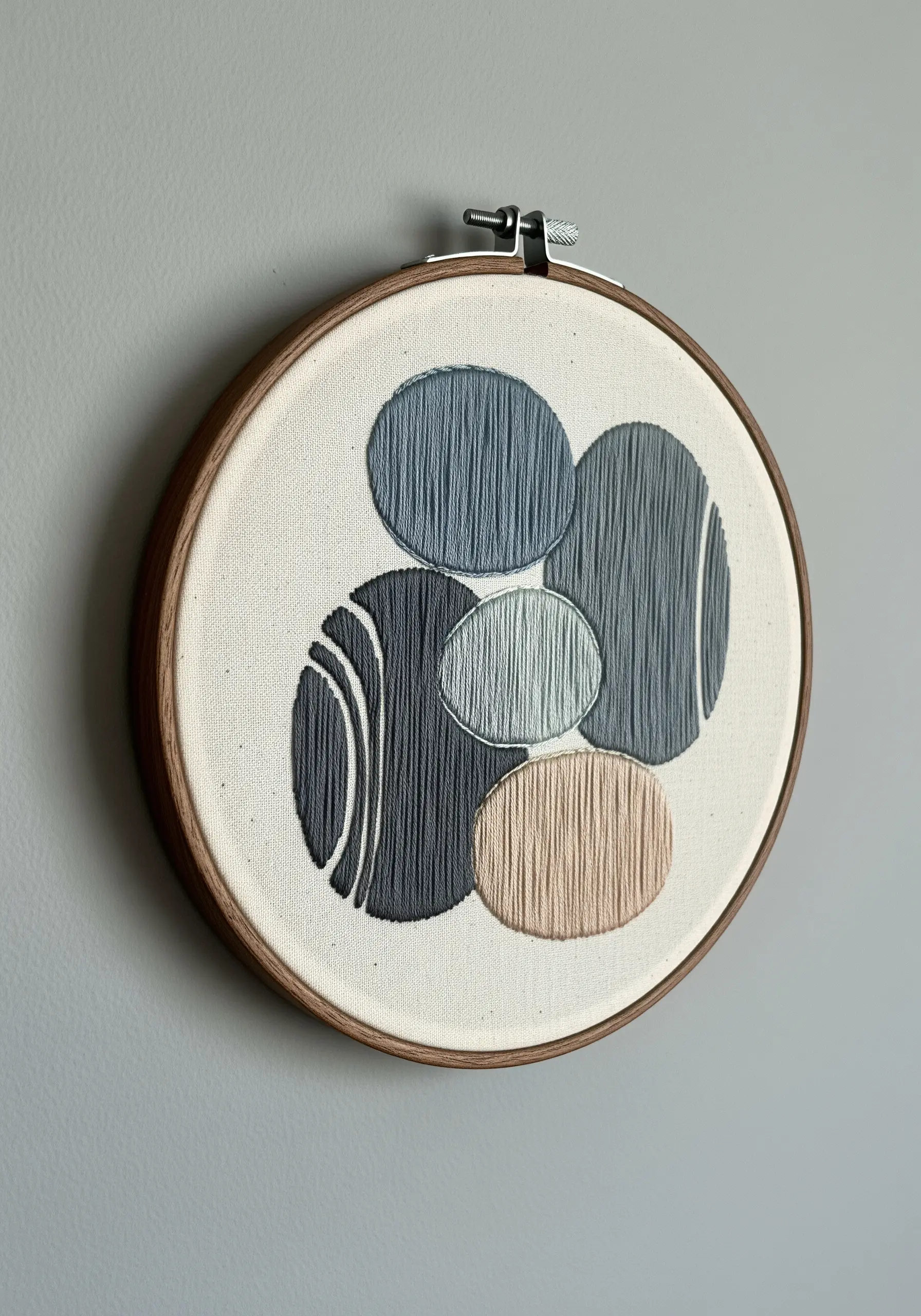 Abstract embroidery of overlapping smooth stones in shades of grey, blue, and blush.