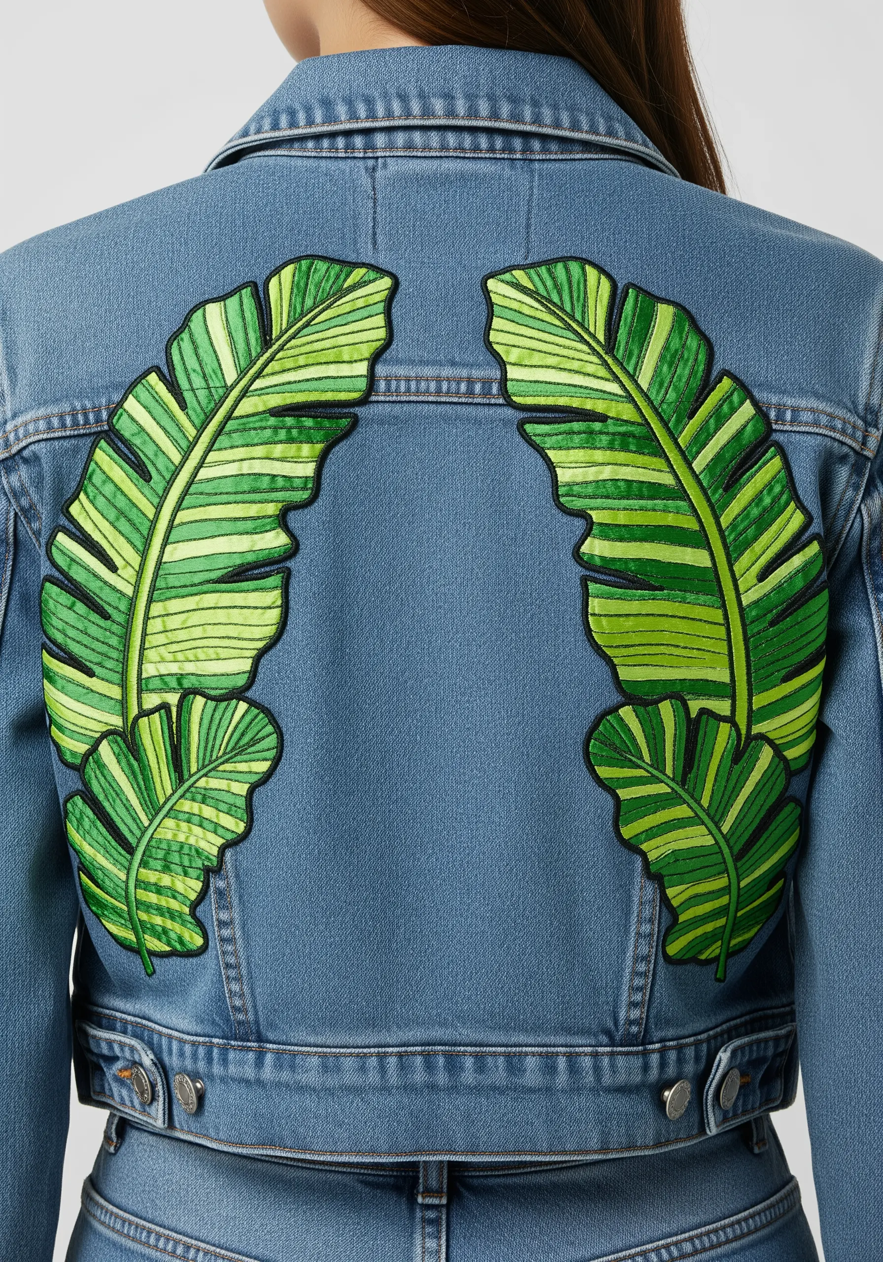 Two large, symmetrical green banana leaves stitched on the back of a denim jacket.