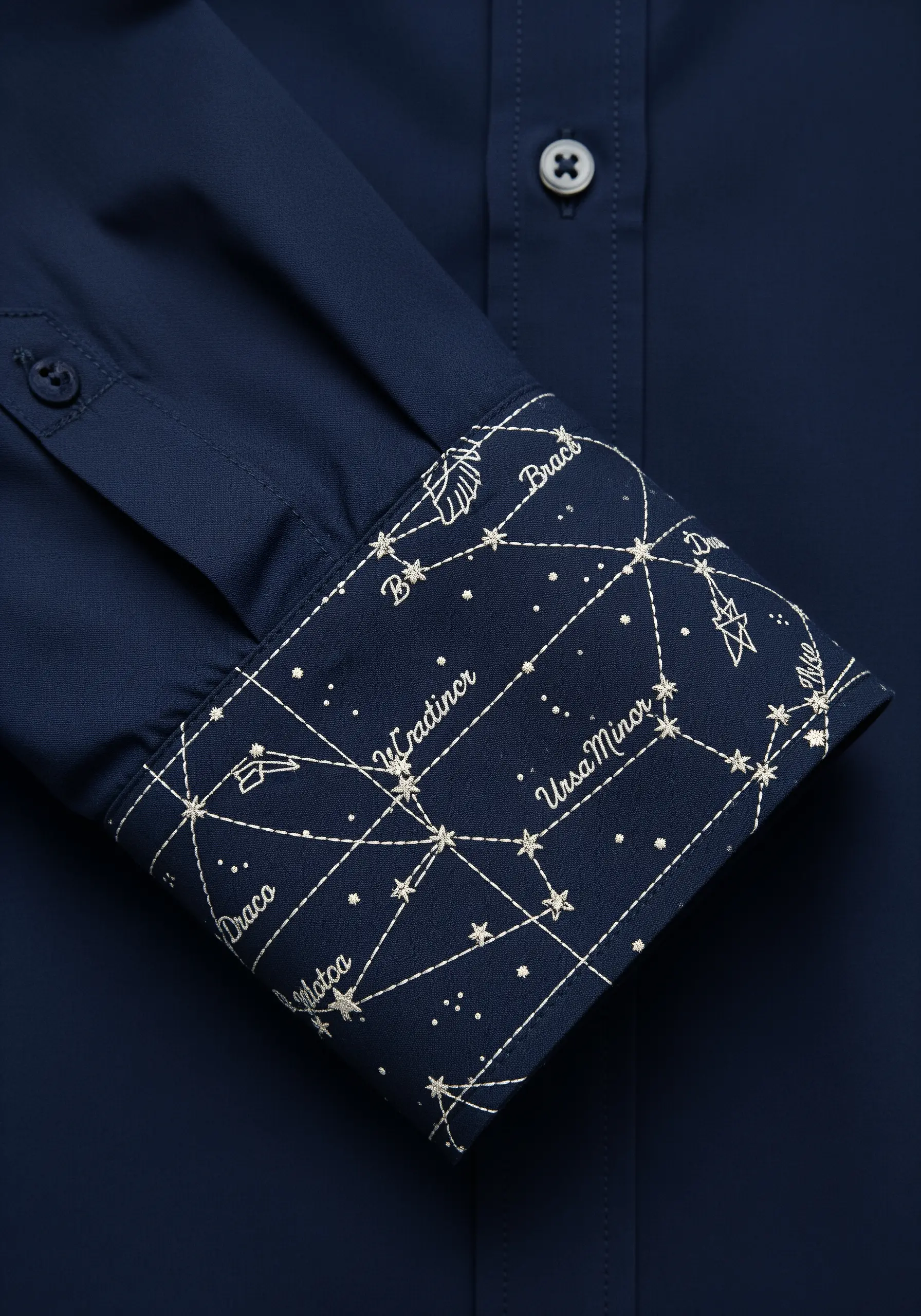Embroidery of star constellations like Ursa Minor and Draco on the inner cuff of a navy blue shirt.