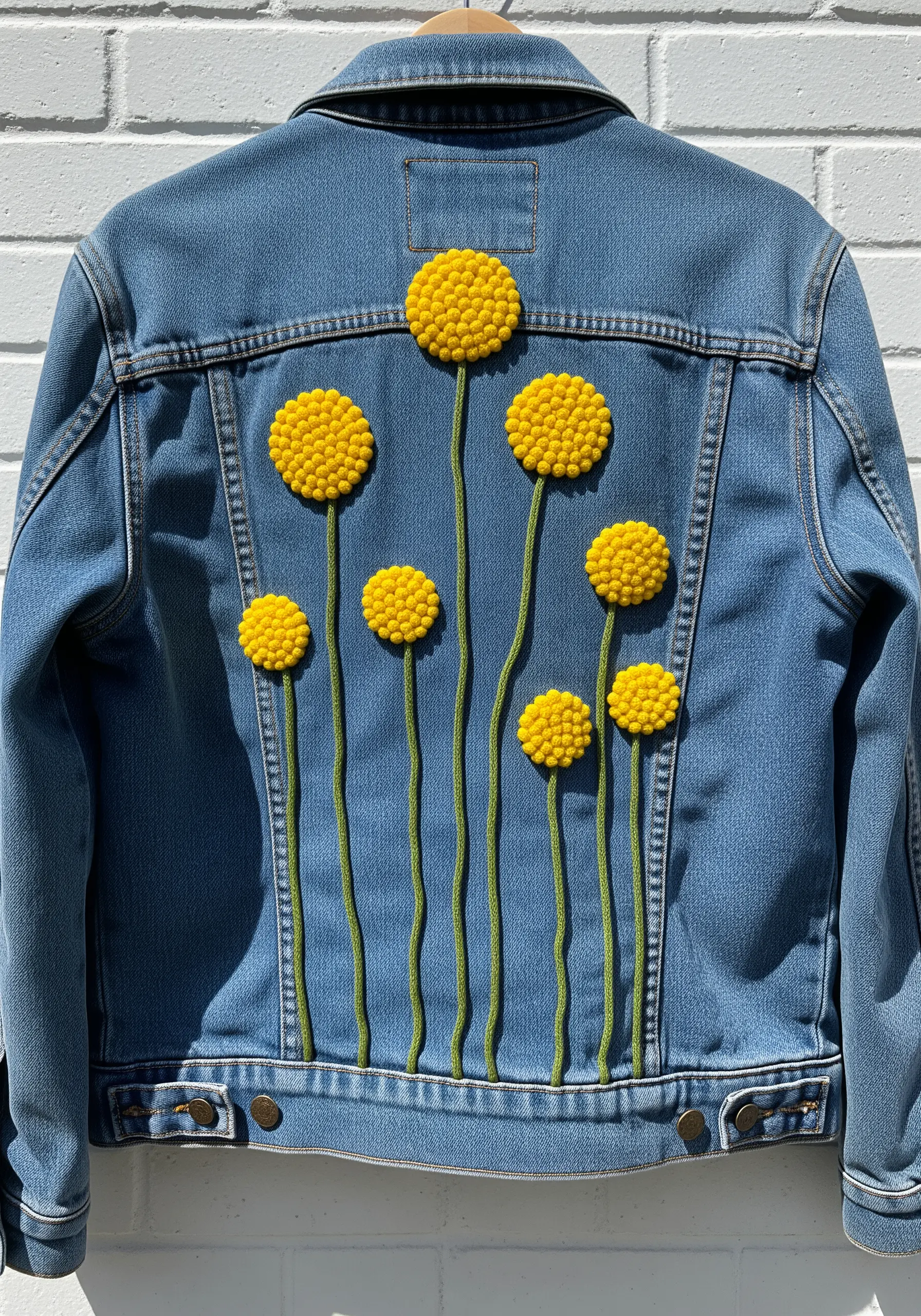 Bright yellow, dimensional craspedia flowers made of French knots embroidered on a denim jacket.