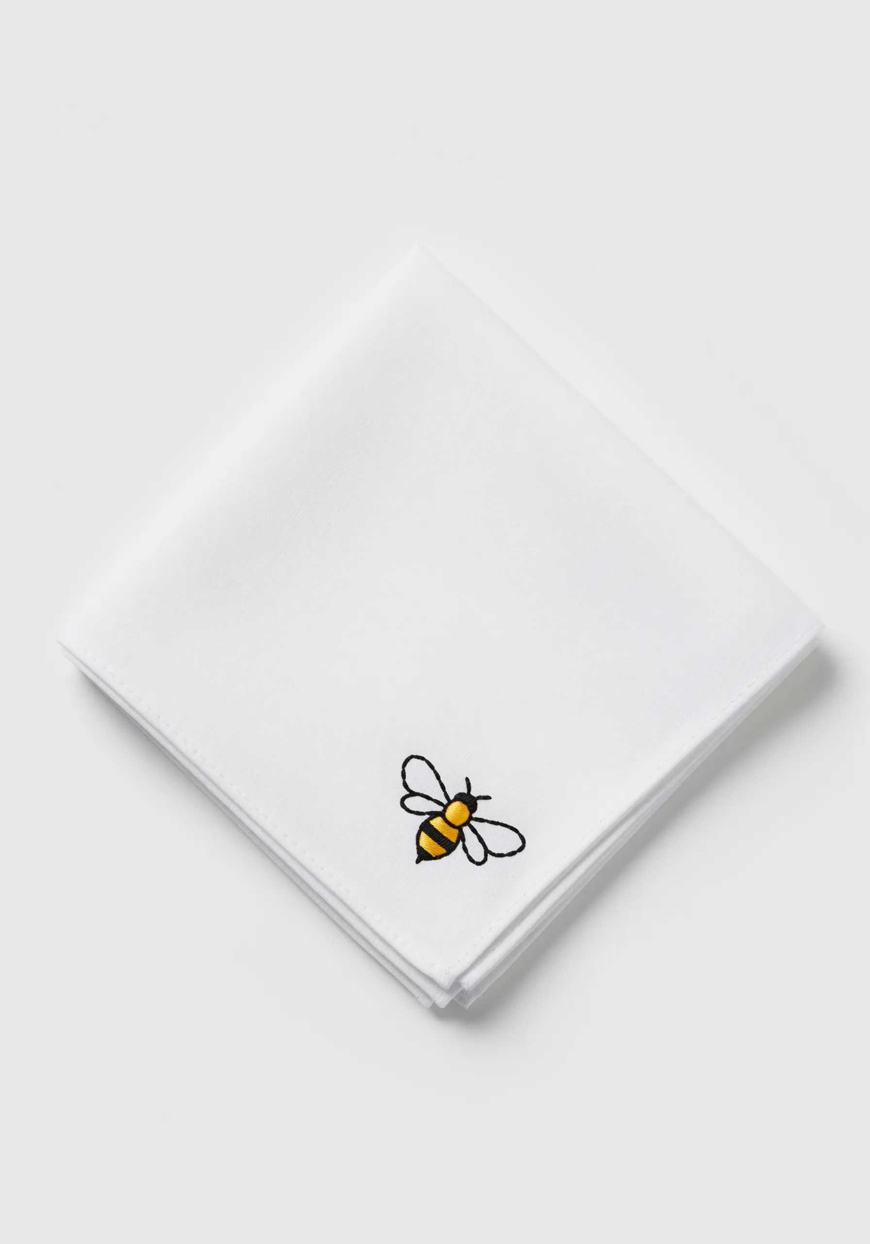 A tiny embroidered bee in the corner of a folded white linen napkin.
