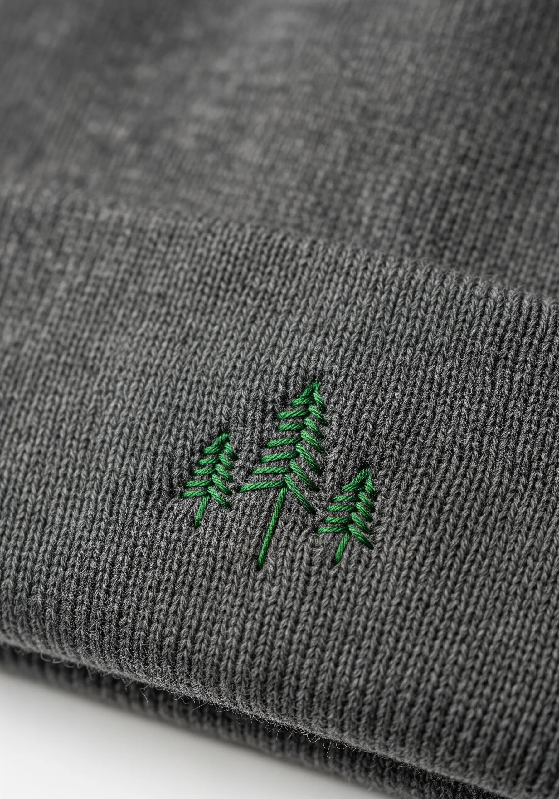 Three small green pine trees embroidered on the cuff of a grey knit beanie.