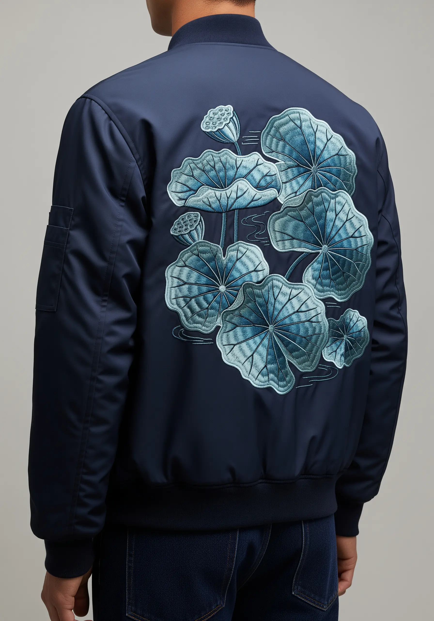 Stylized lotus pads embroidered in shades of blue on the back of a navy bomber.