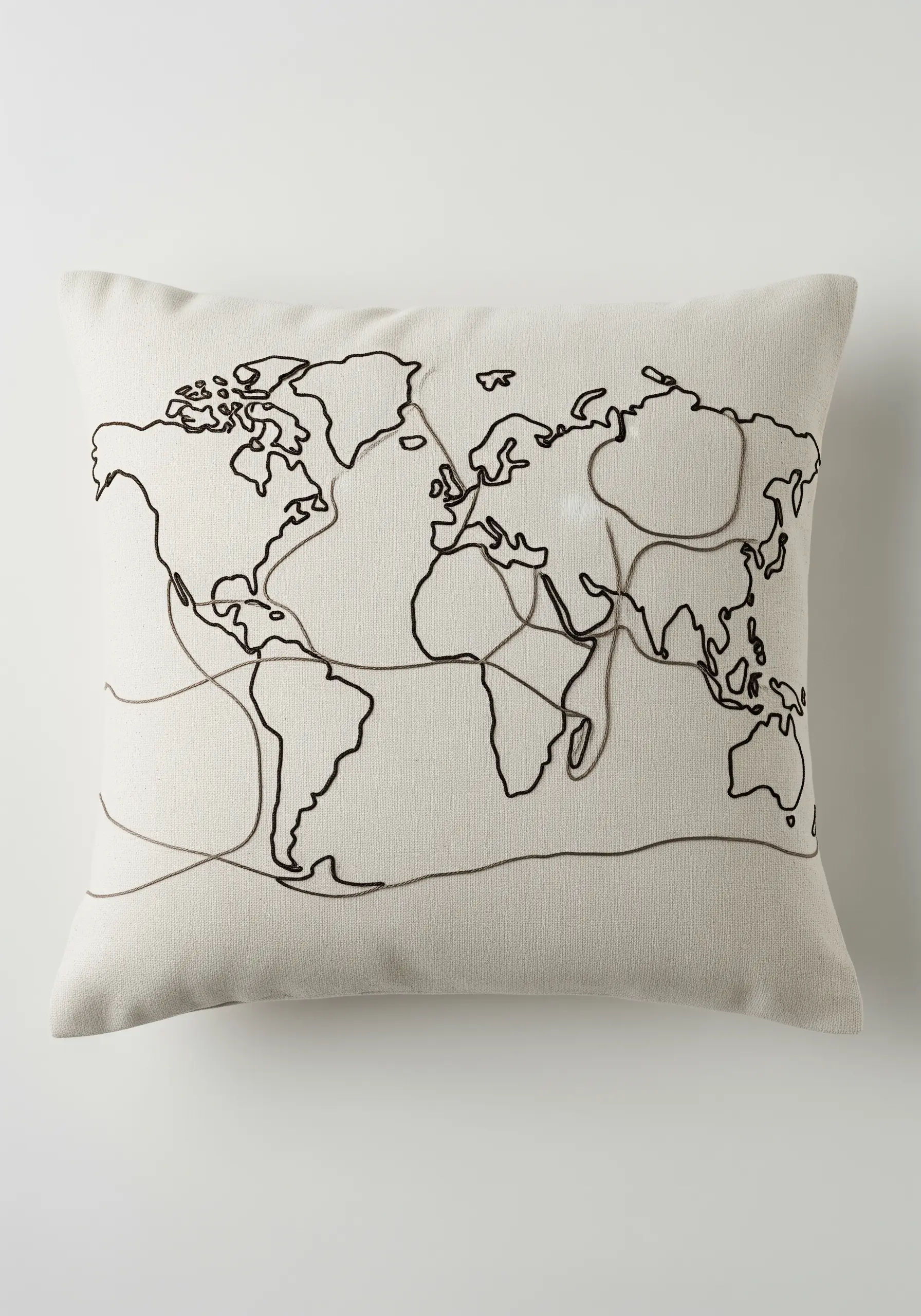 A world map in black outline with lighter intersecting lines stitched on a neutral cushion.