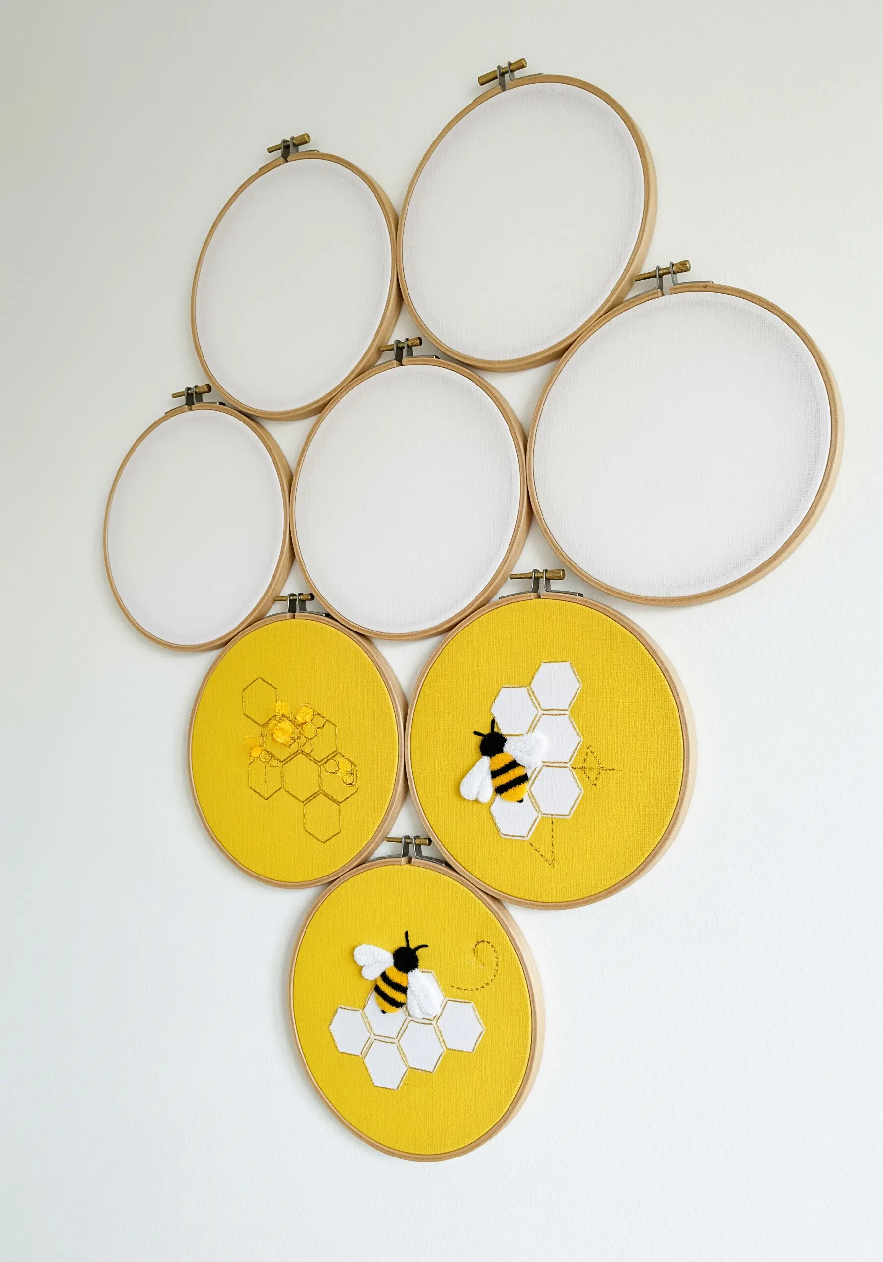 A cluster of embroidery hoops on a wall, some empty and some with bee and honeycomb designs.