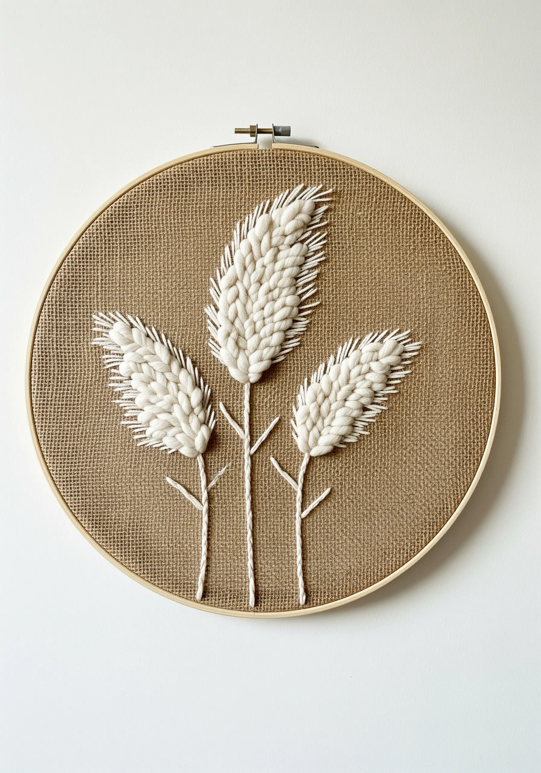 Three stems of pampas grass stitched with thick white yarn on a piece of burlap in a hoop.