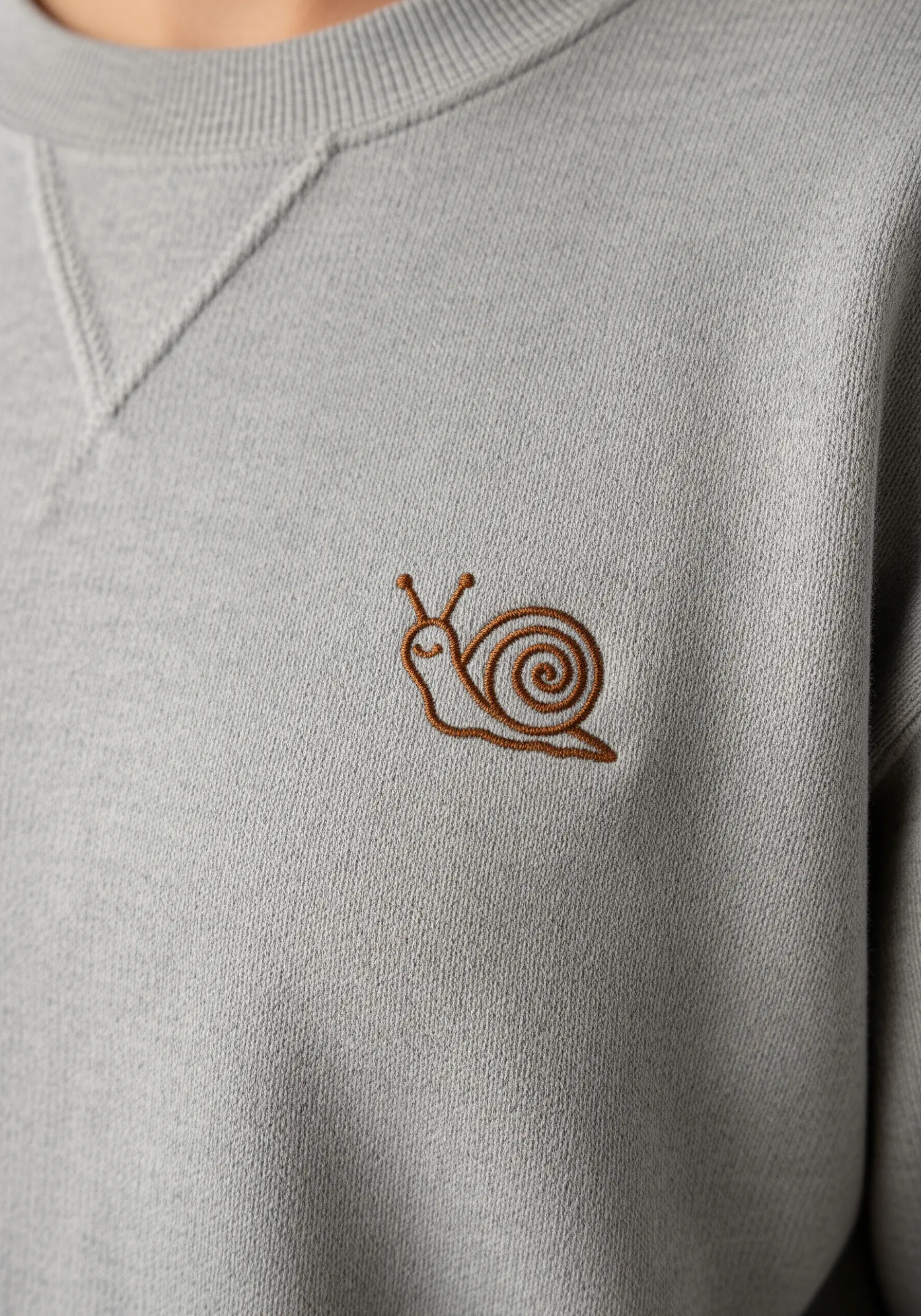Simple brown outline of a snail embroidered on the chest of a grey sweatshirt.