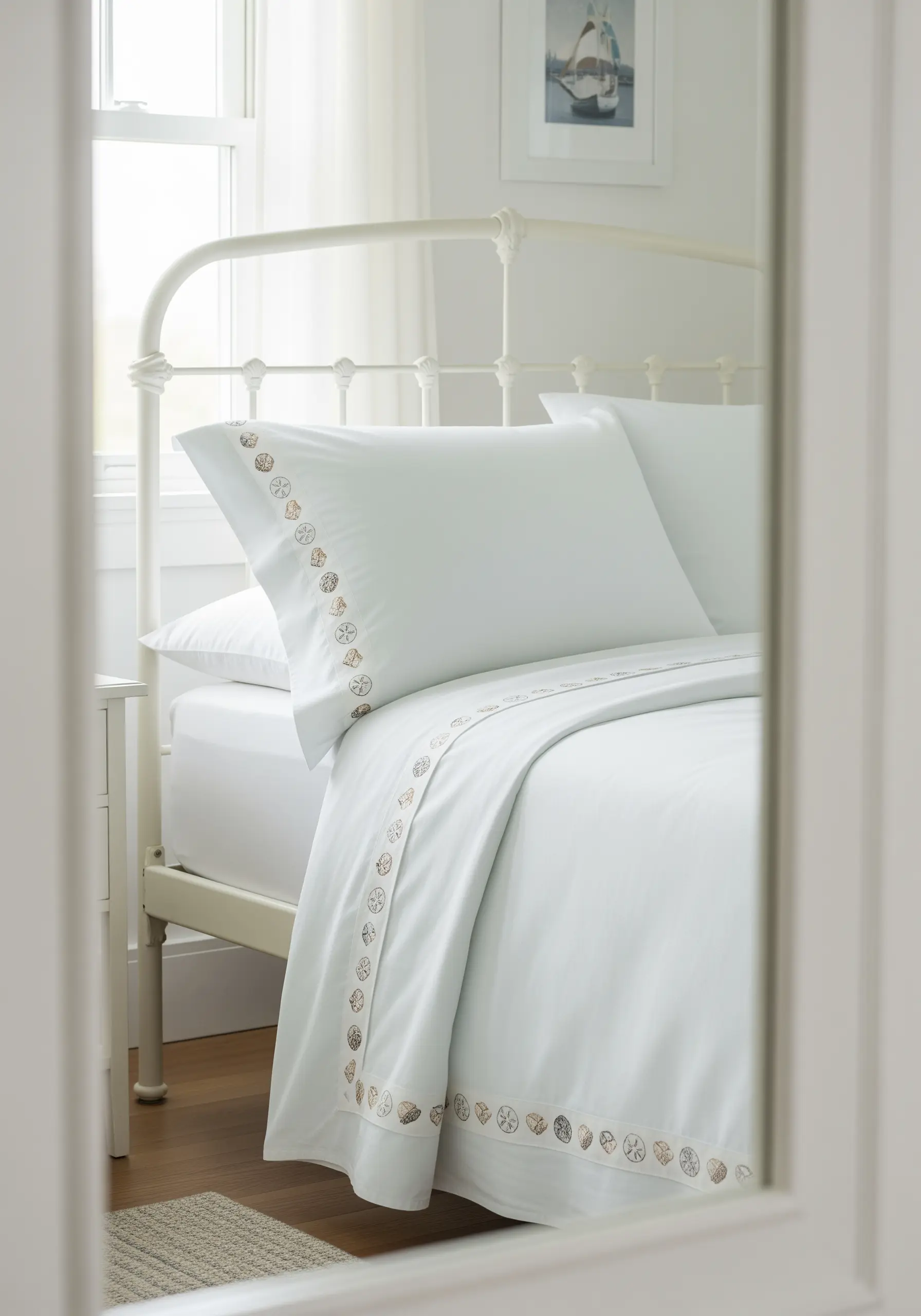 A border of varied seashell motifs embroidered in neutral tones on pale blue sheets.
