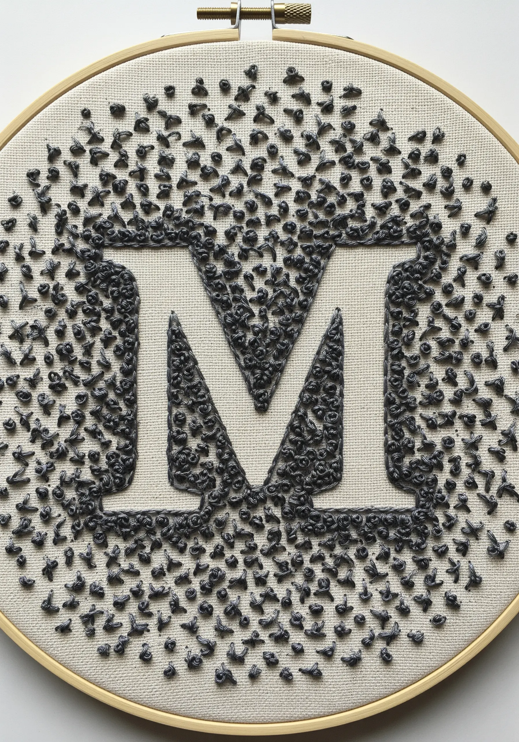 Monogram 'M' created with dense and scattered charcoal French knots.