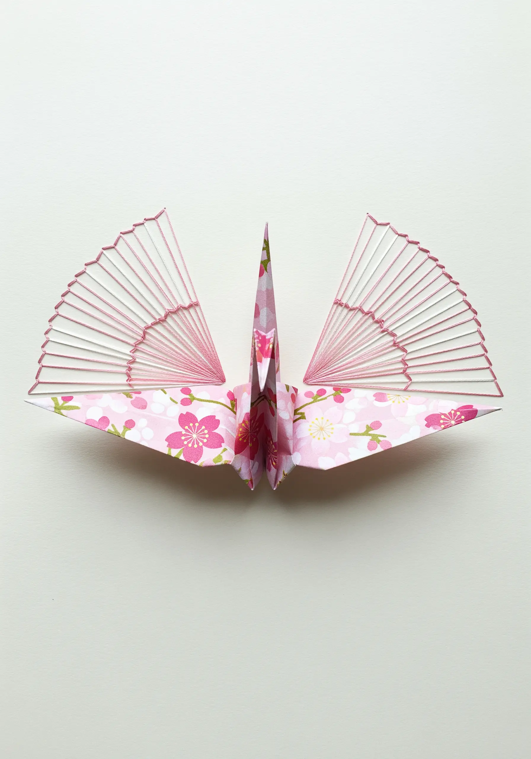 A pink floral origami crane with delicate radiating stitches embroidered on its wings.