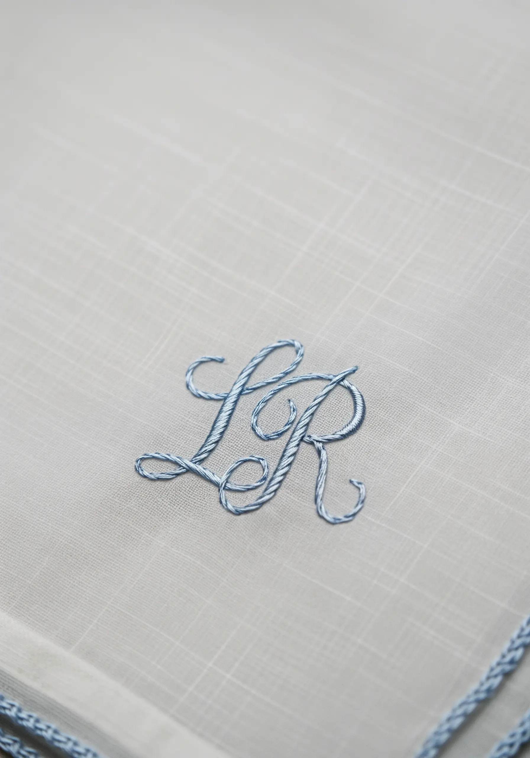 Interlocking script 'LR' monogram in padded blue satin stitch on a fine linen handkerchief.