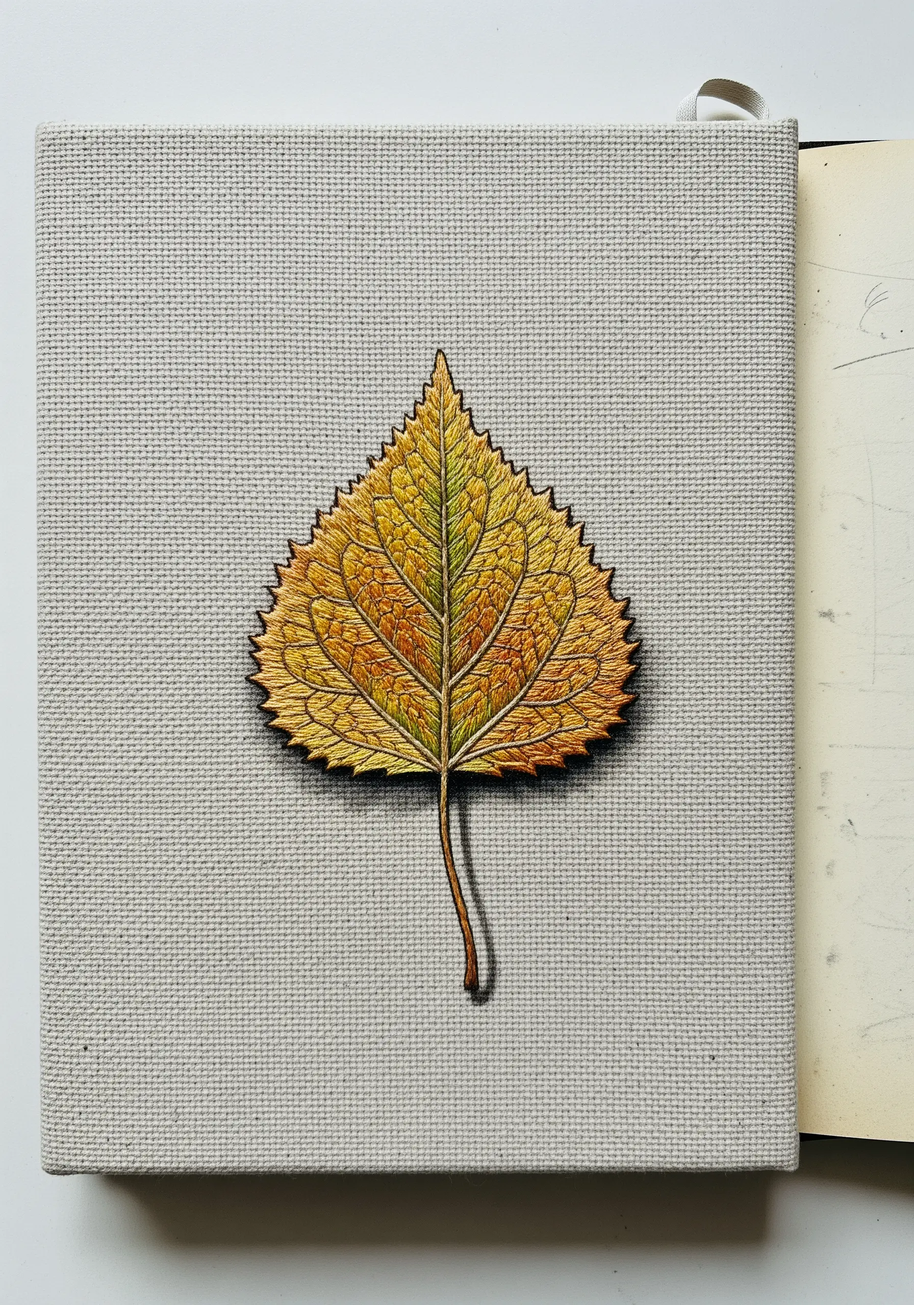 A hyperrealistic embroidered autumn leaf with detailed thread painting on a canvas journal.