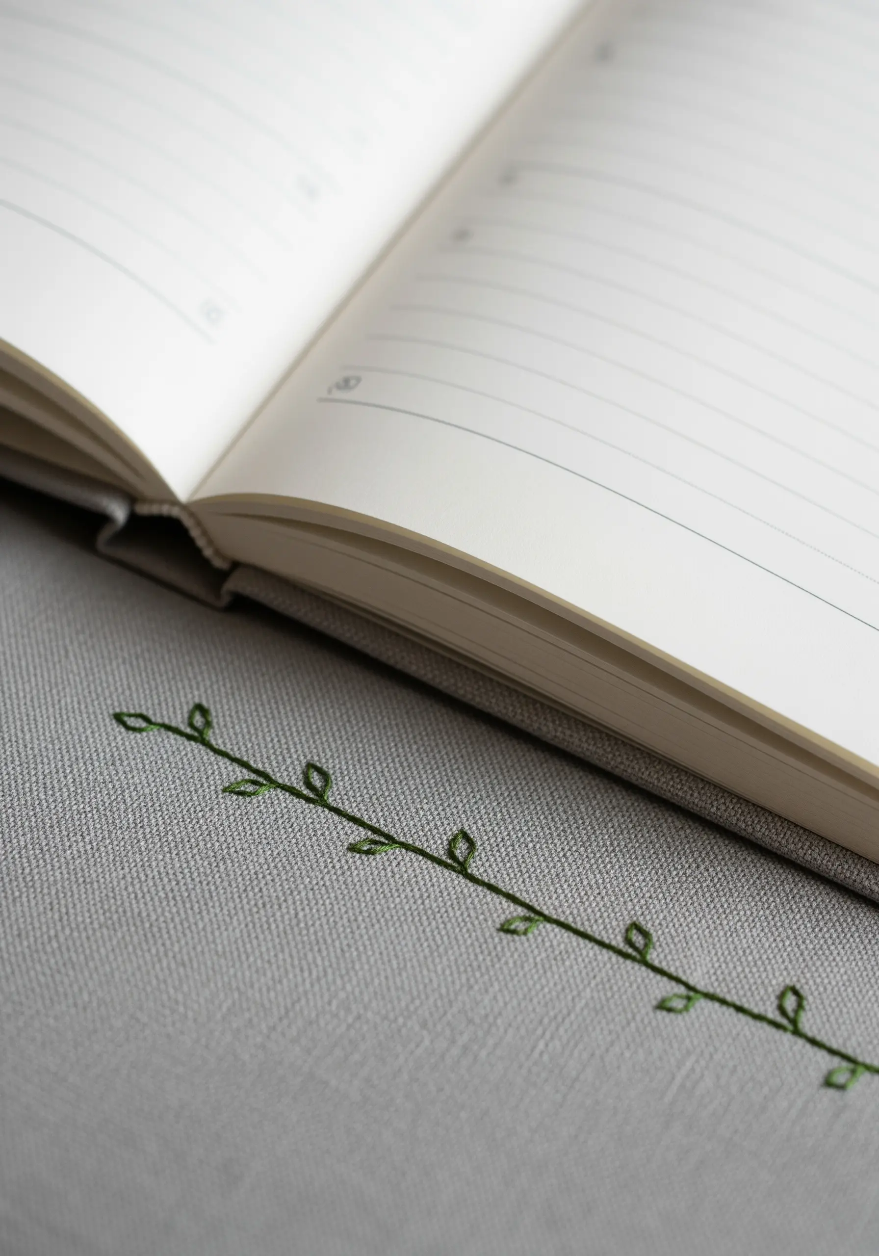 A very simple, minimalist embroidered vine with open-outline leaves on a grey book cover.