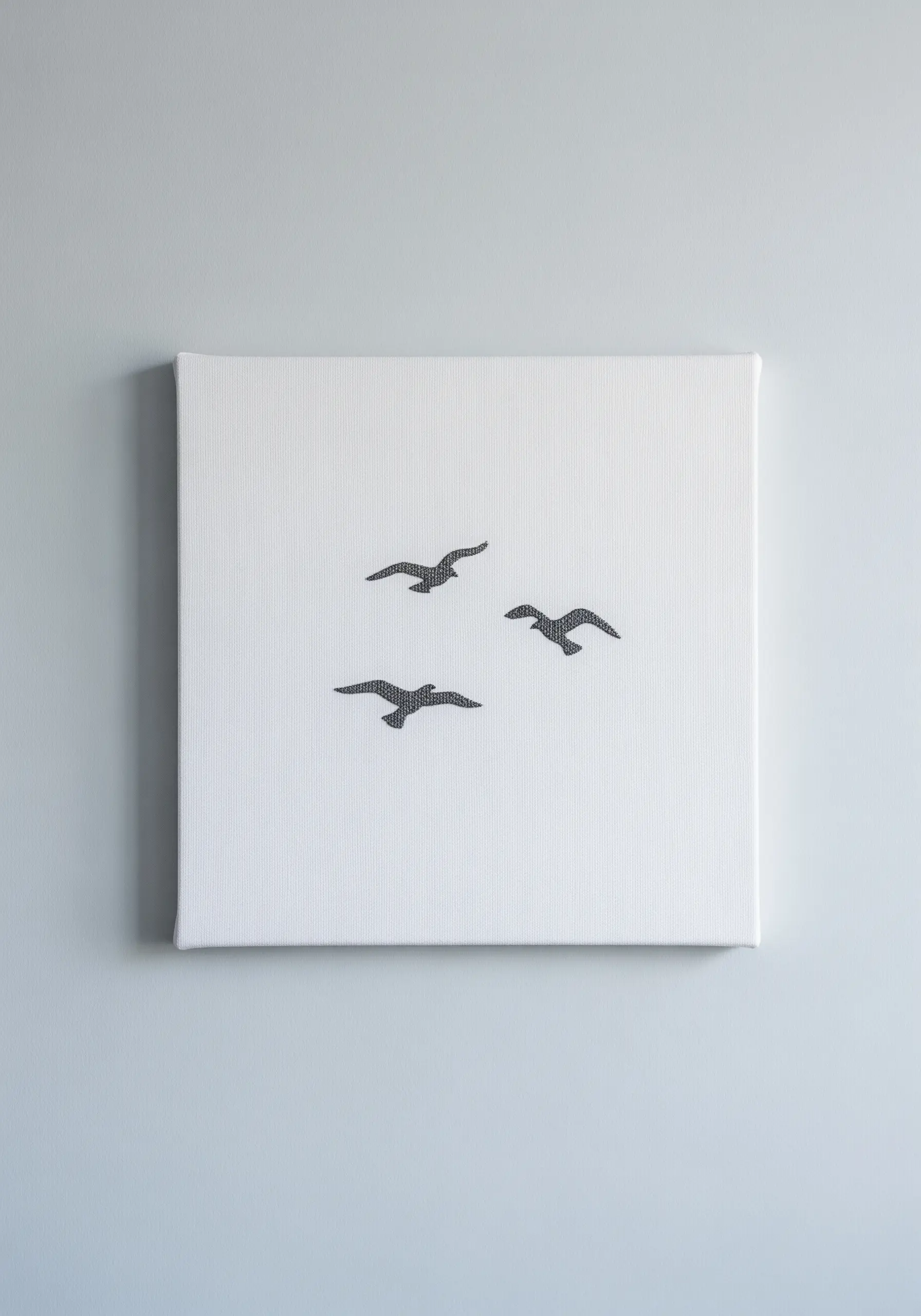Three small embroidered birds in flight on a stark white canvas.