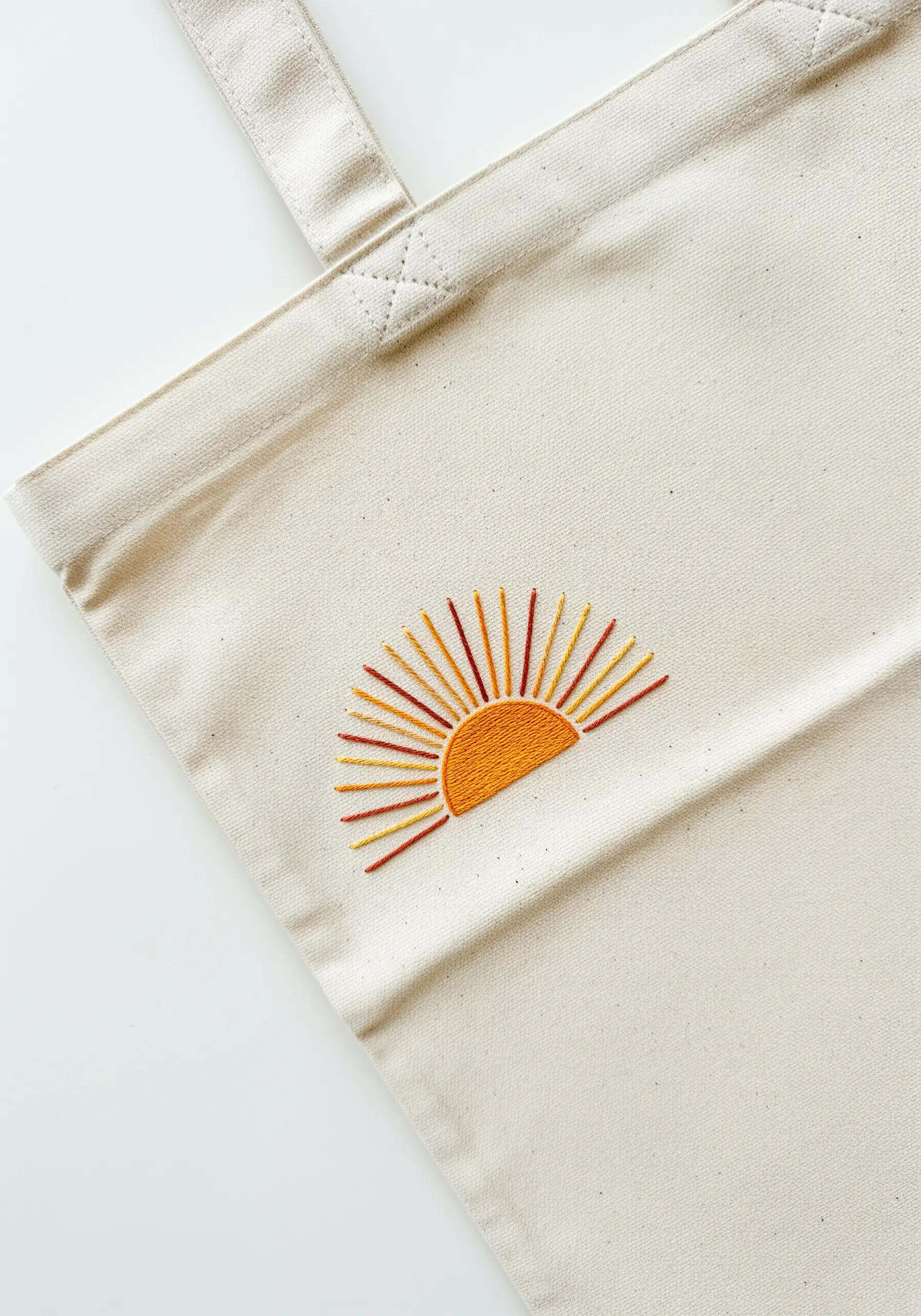 Minimalist sunrise embroidery with orange and yellow rays on a canvas tote bag.