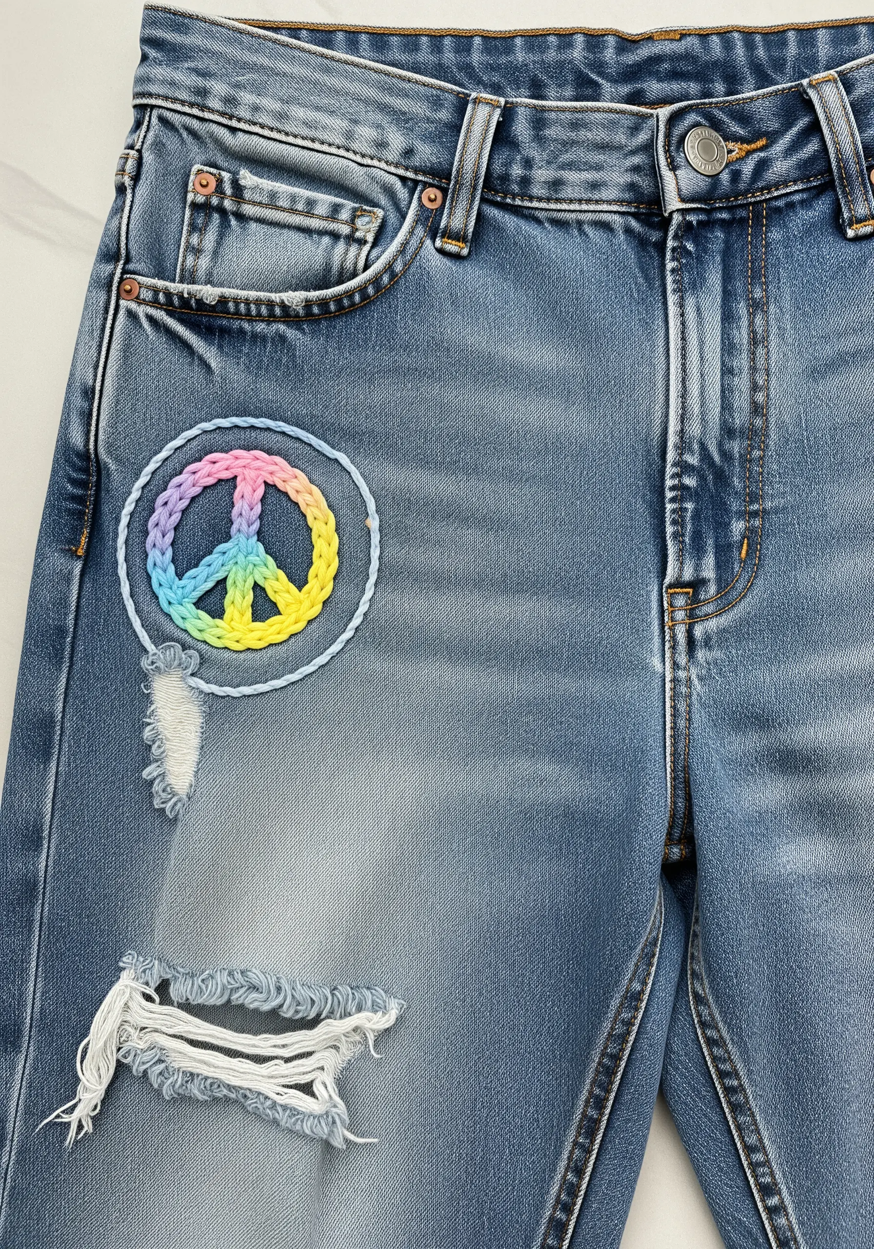 A peace sign embroidered with a pastel rainbow gradient and a braided border.