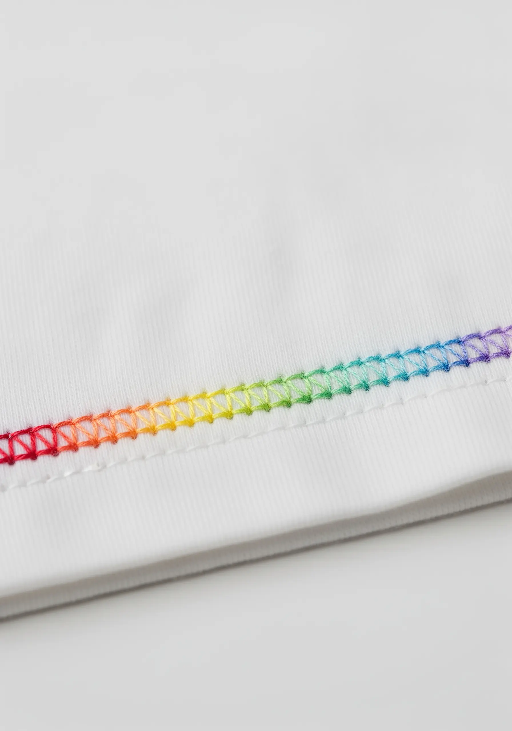 A colorful blanket stitch in a rainbow gradient along the hem of a white shirt.