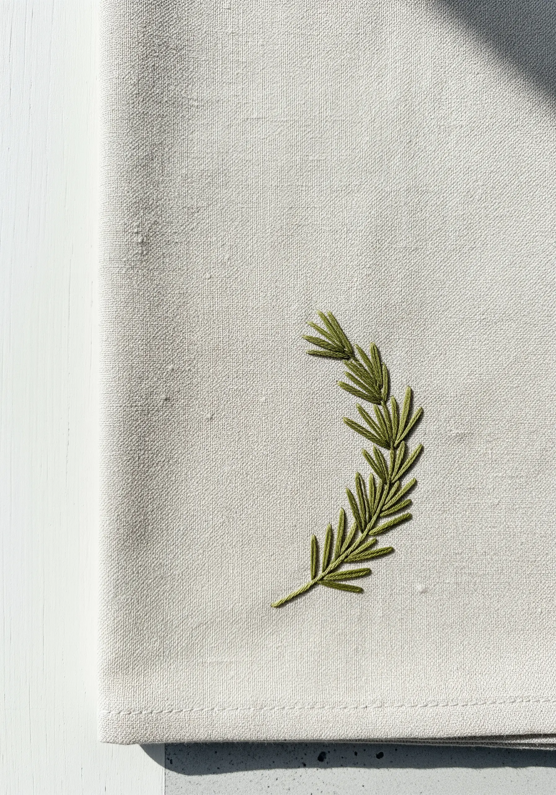Hand-embroidered rosemary sprig in olive green on a natural linen napkin.