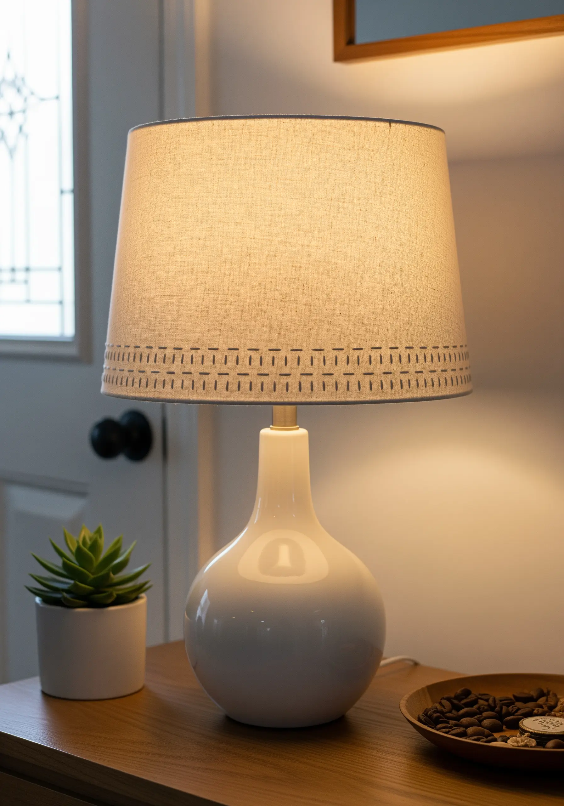 A close-up of a linen lampshade with a simple running stitch border in grey thread.