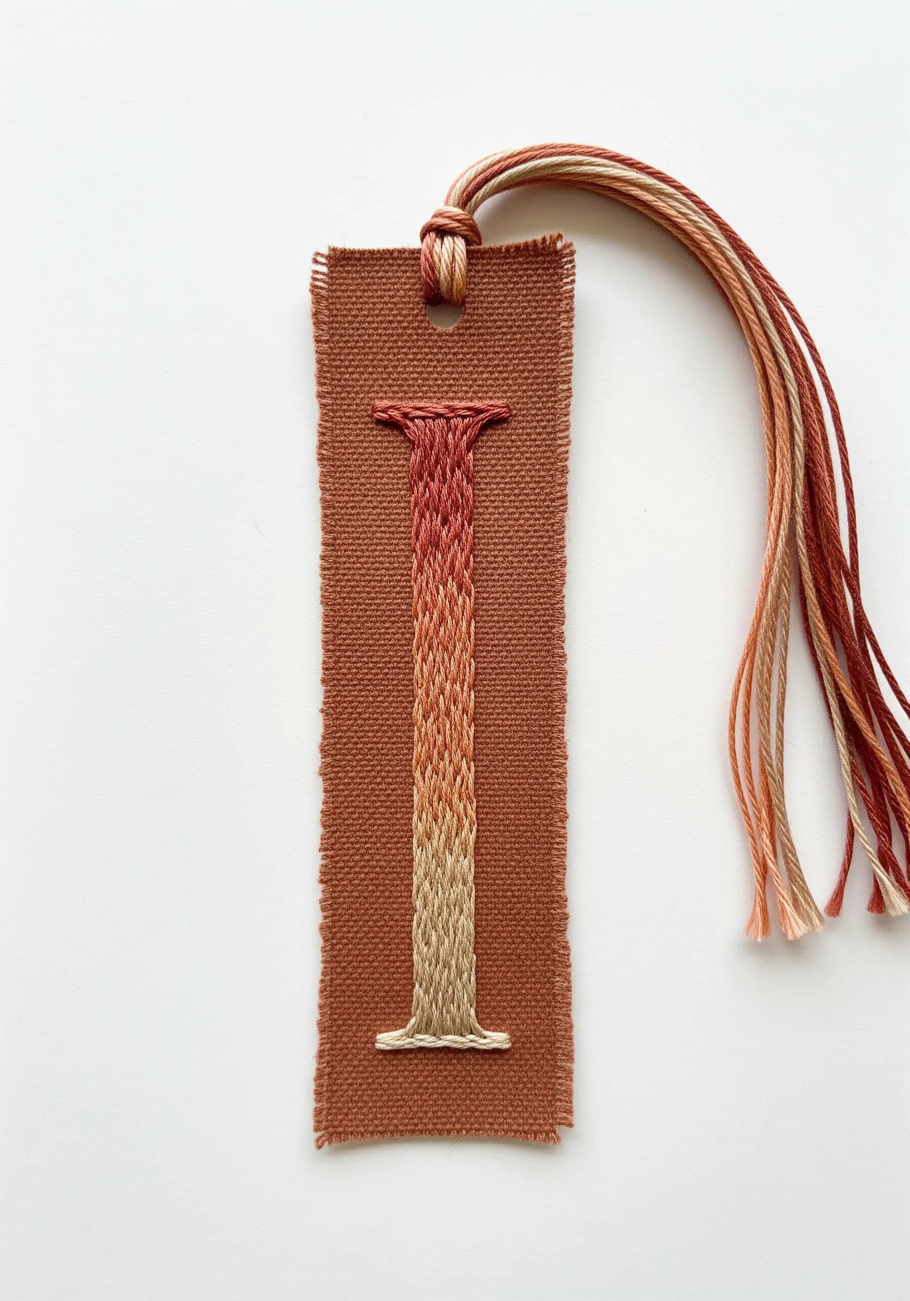 Monogram 'I' on a fabric bookmark with a vertical red-to-beige ombré effect.