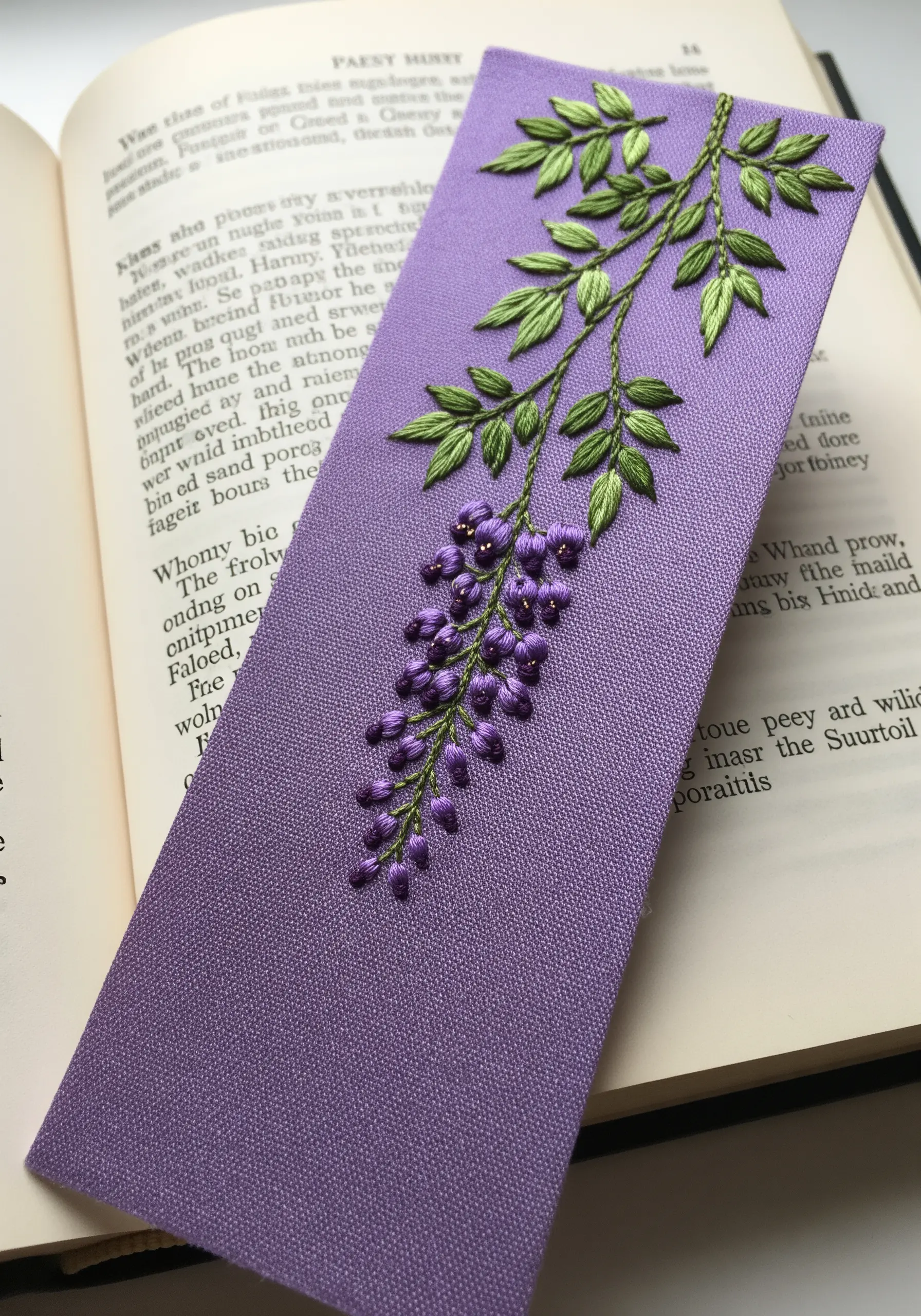 An elegant wisteria branch embroidered on a purple bookmark with French knot blossoms.