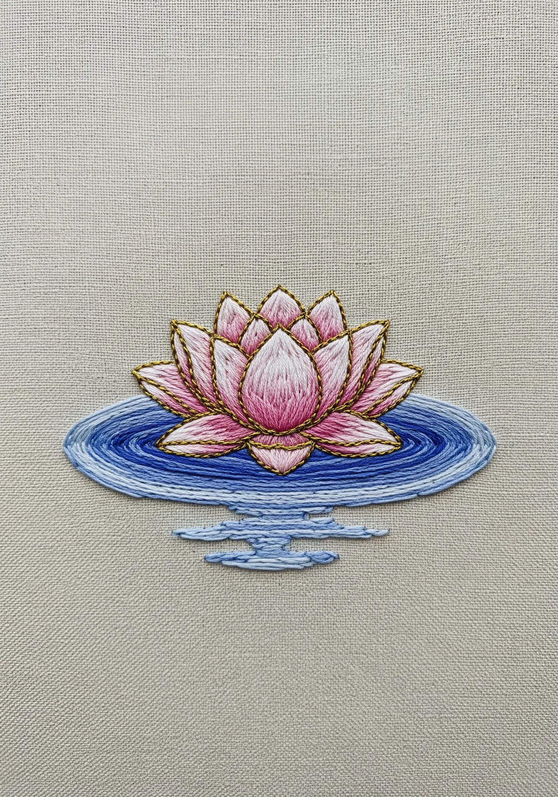 A thread-painted pink water lily with a gold outline, floating on blue water.