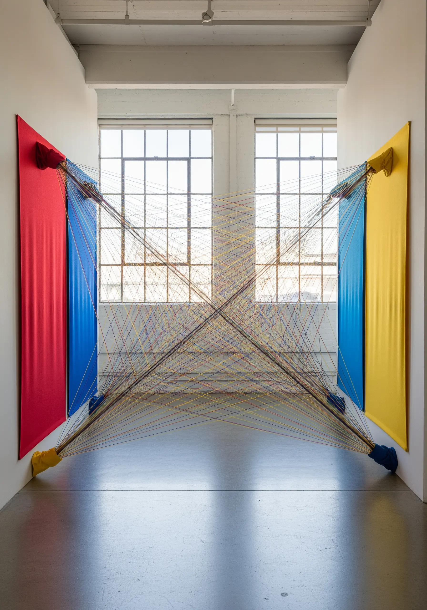 A room-scale string art installation with threads stretching between colorful fabric panels on walls.