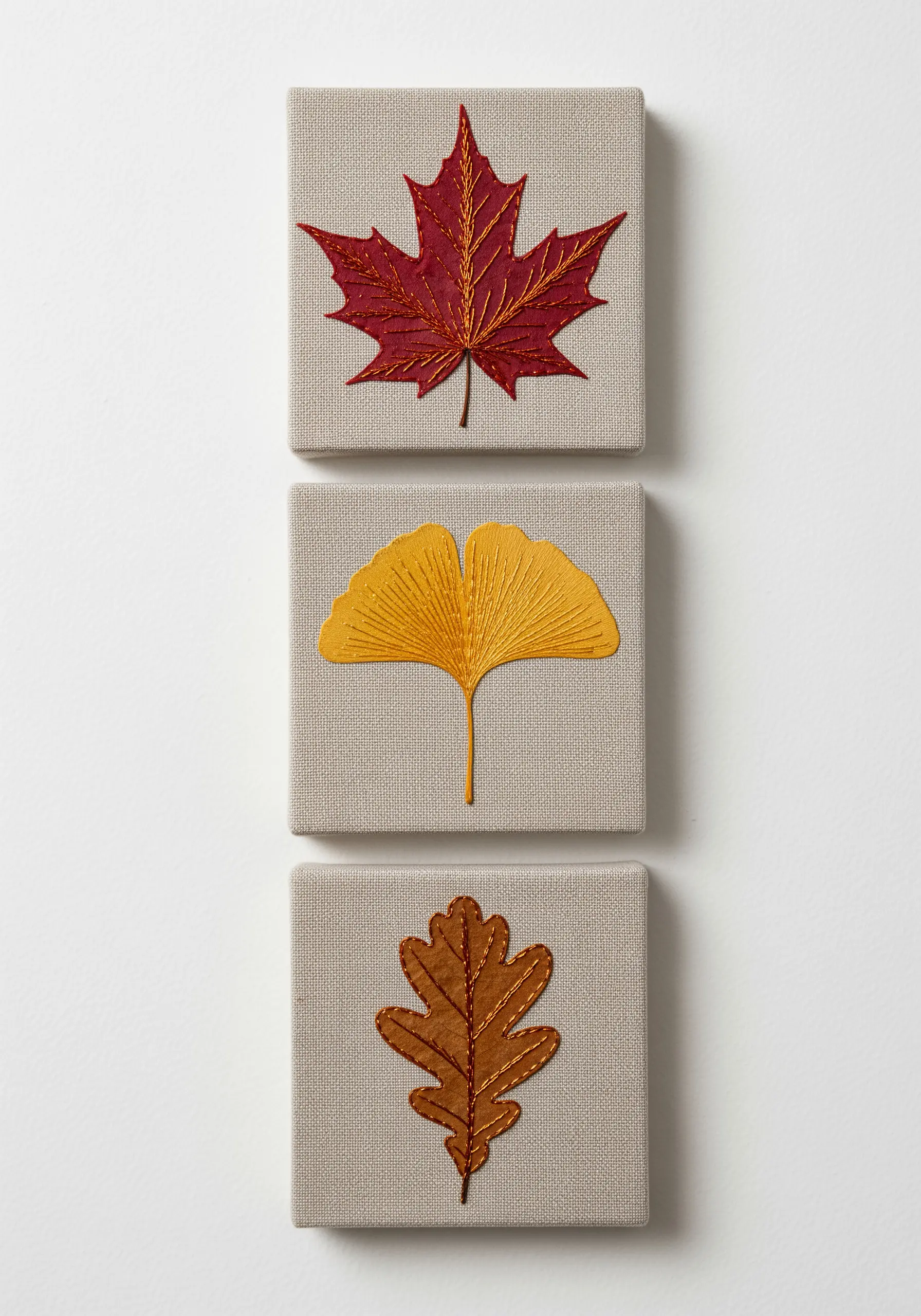 Three small canvases, each with an embroidered autumn leaf in red, yellow, and brown.