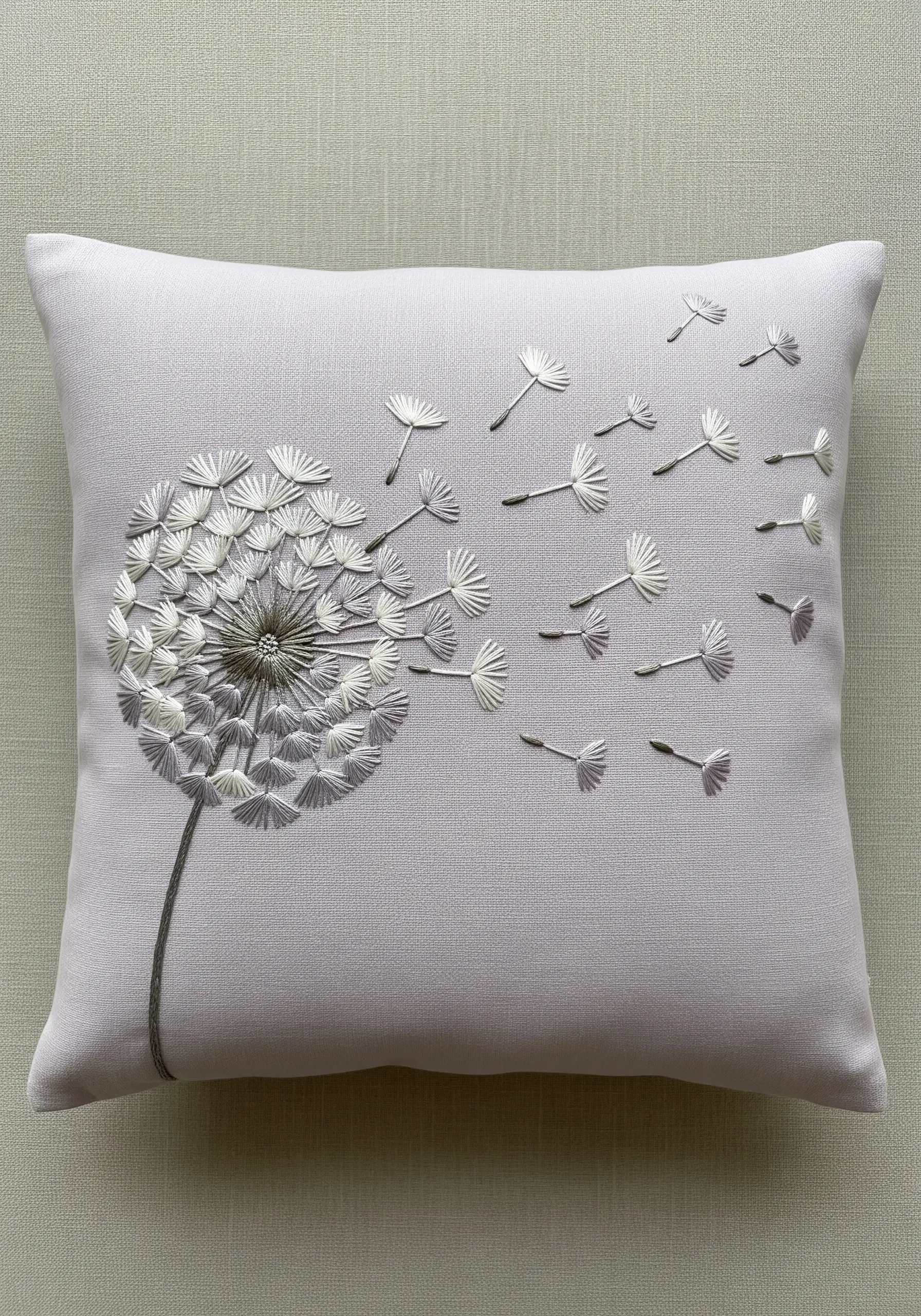 A dandelion puff embroidered in a subtle white-to-grey gradient on a light grey cushion.