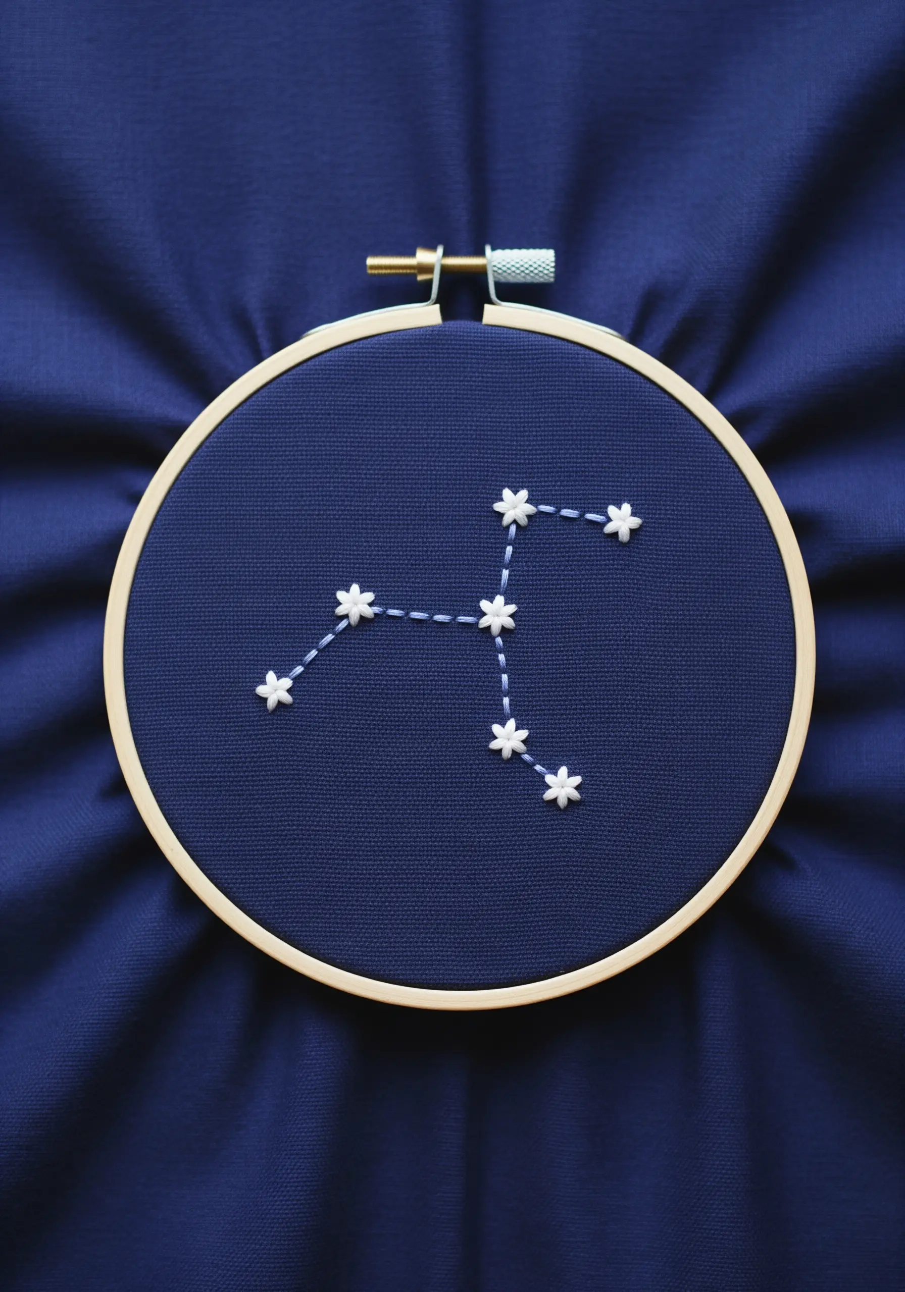 An embroidered constellation with white French knot stars on a deep blue fabric.