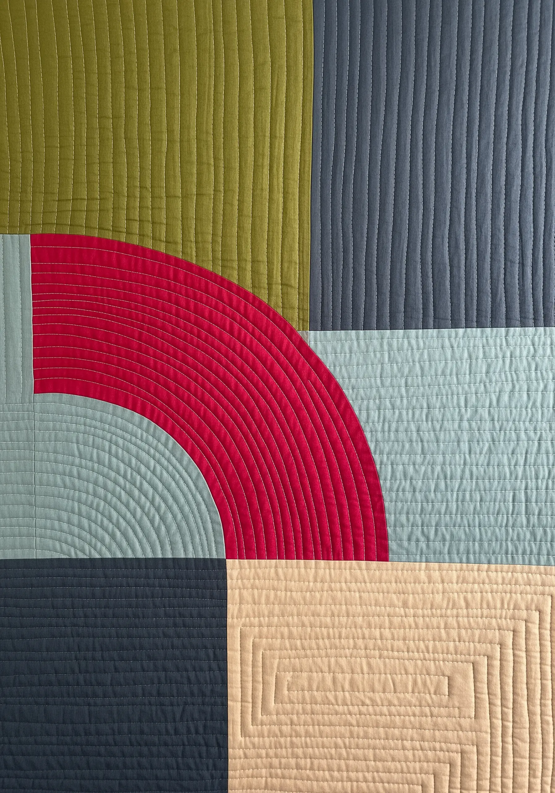 Close-up of a modern quilt with varied stitching patterns on solid color blocks.