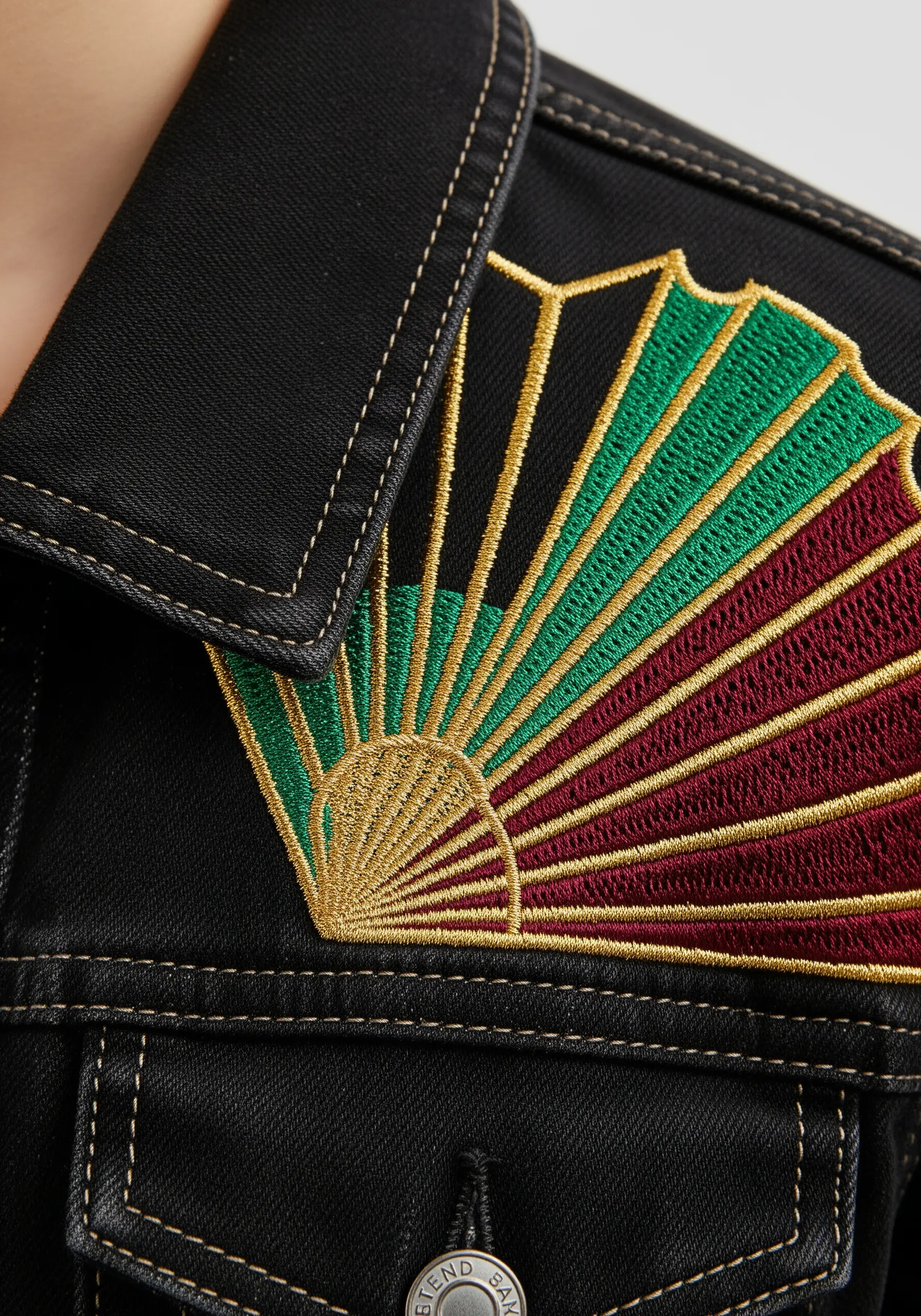 An embroidered fan design with radiating satin stitches in green, red, and gold.
