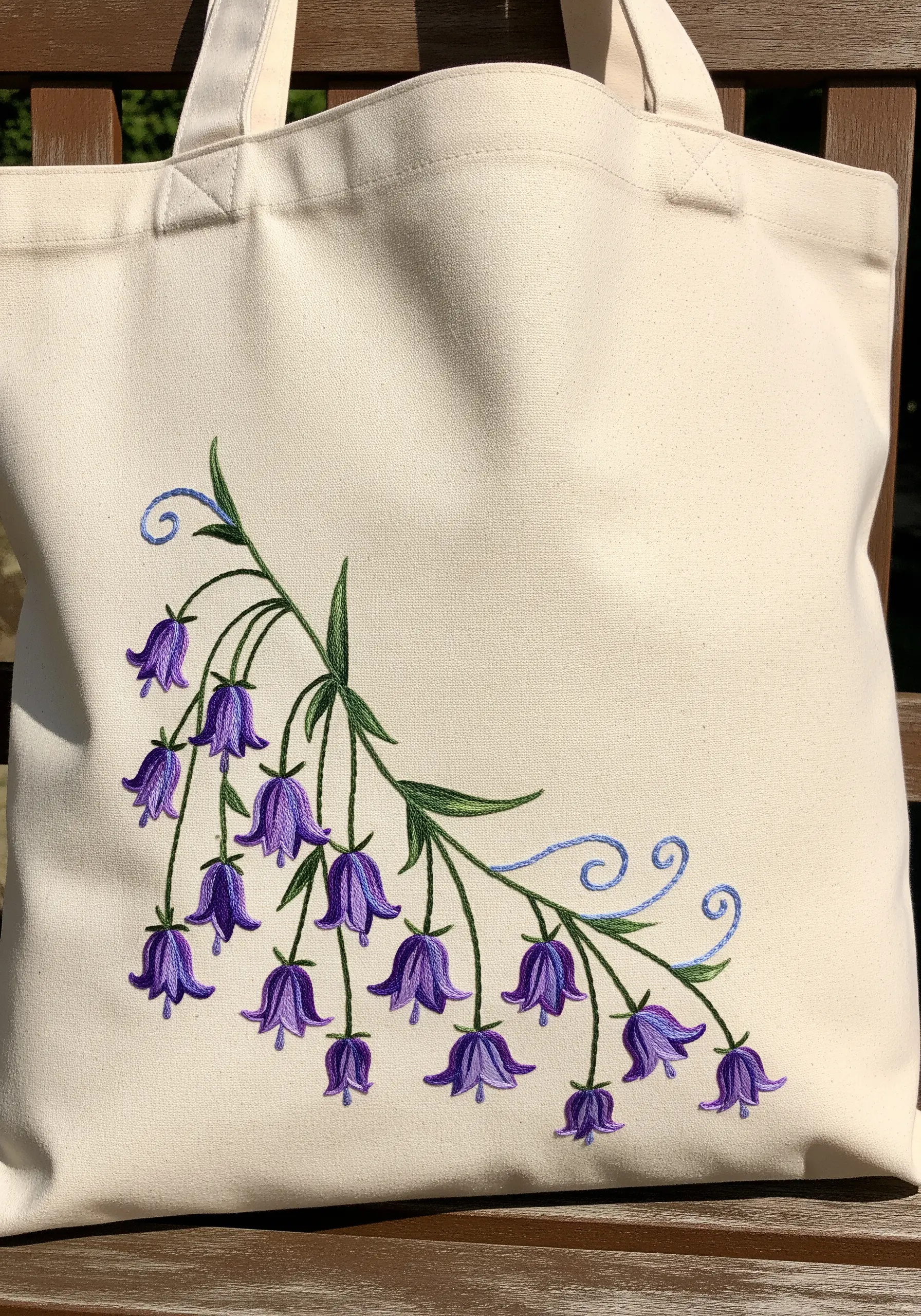 A delicate branch of embroidered purple bluebell flowers on a canvas tote bag