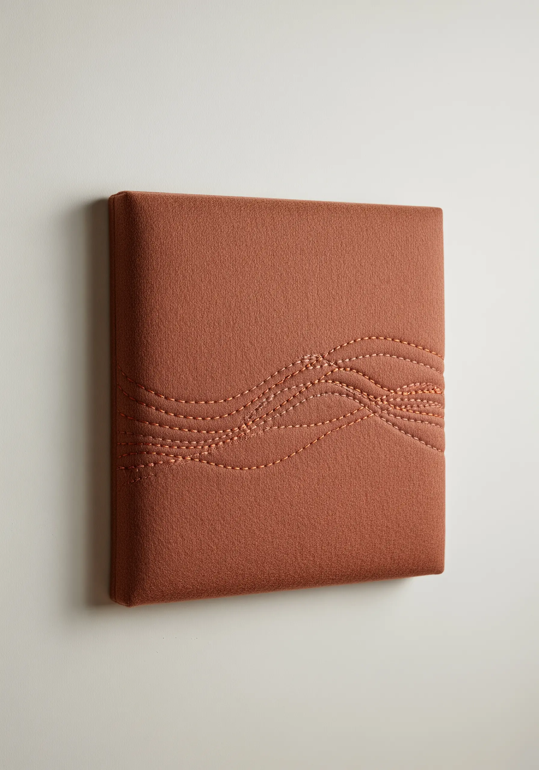 A padded terracotta-colored wall panel with intersecting wavy lines of running stitch embroidery.