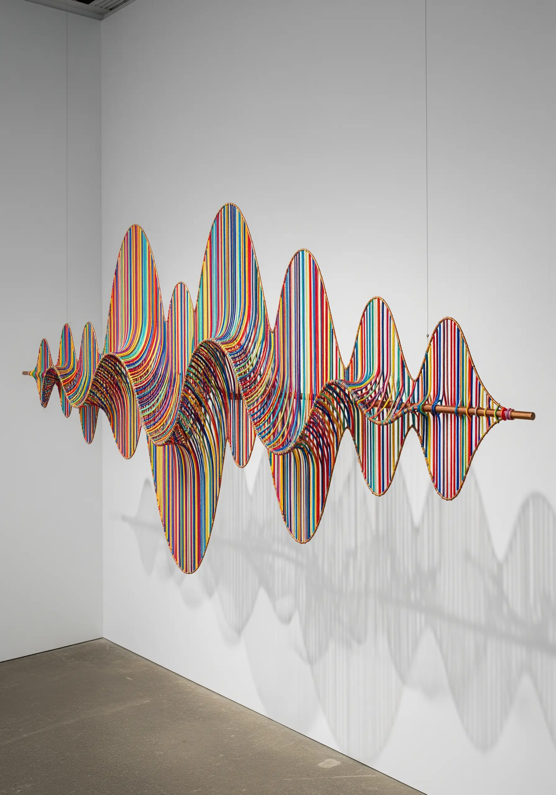 A colorful, undulating soundwave sculpture made from hundreds of stretched vertical threads.