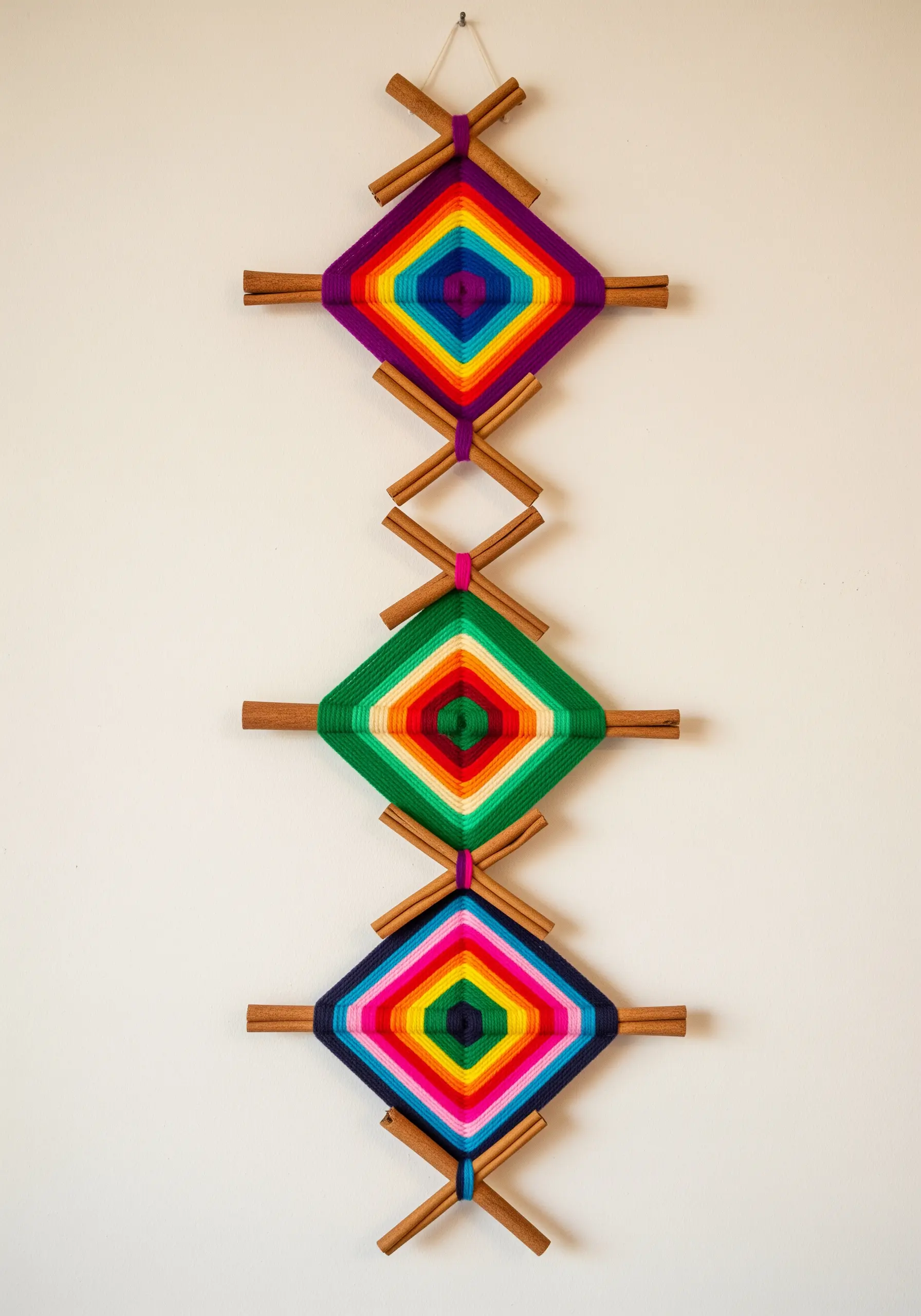 A trio of colorful Ojo de Dios weavings made with yarn and cinnamon sticks.