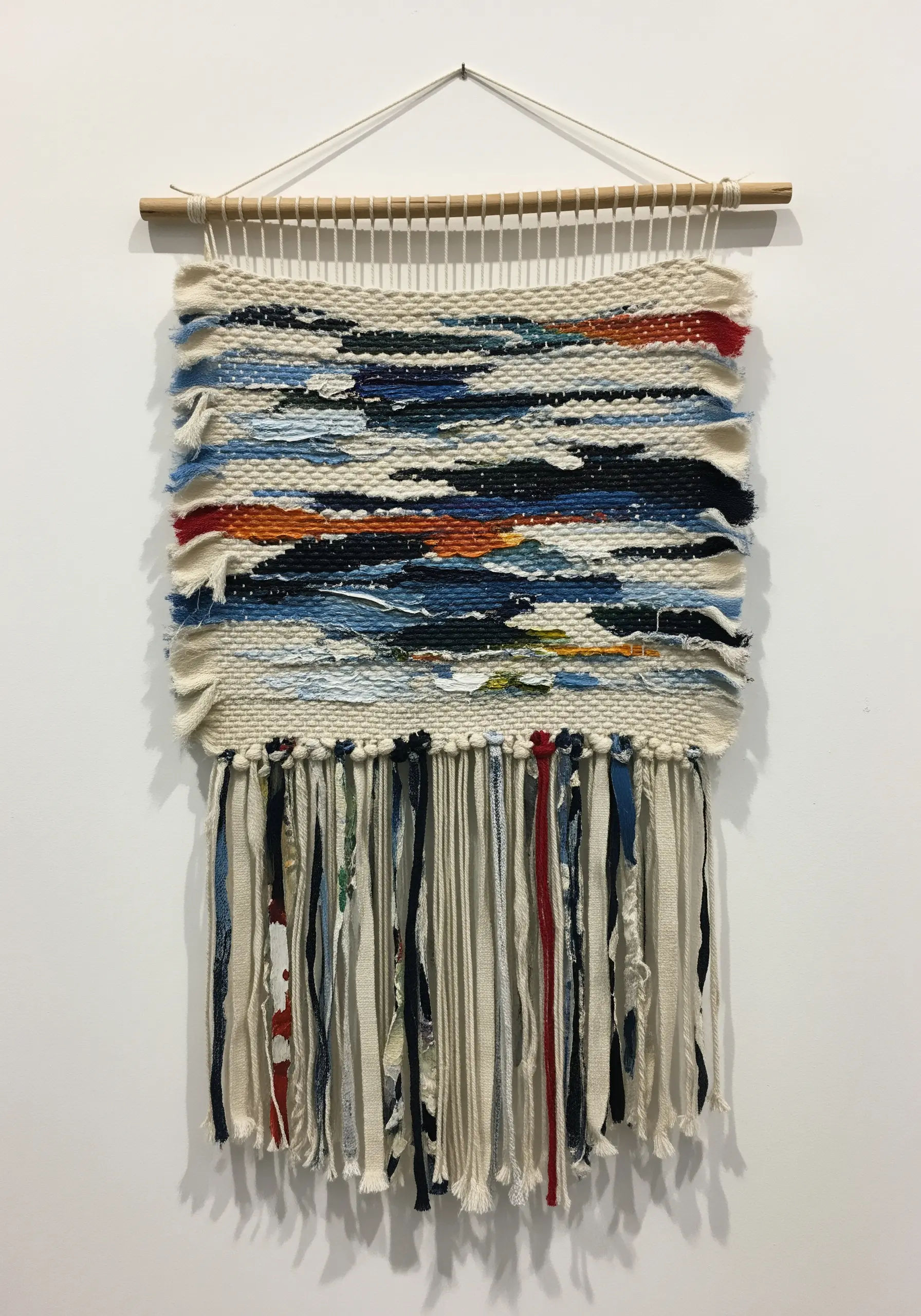 A small, abstract woven wall hanging with a chaotic mix of colors, textures, and fabric scraps.