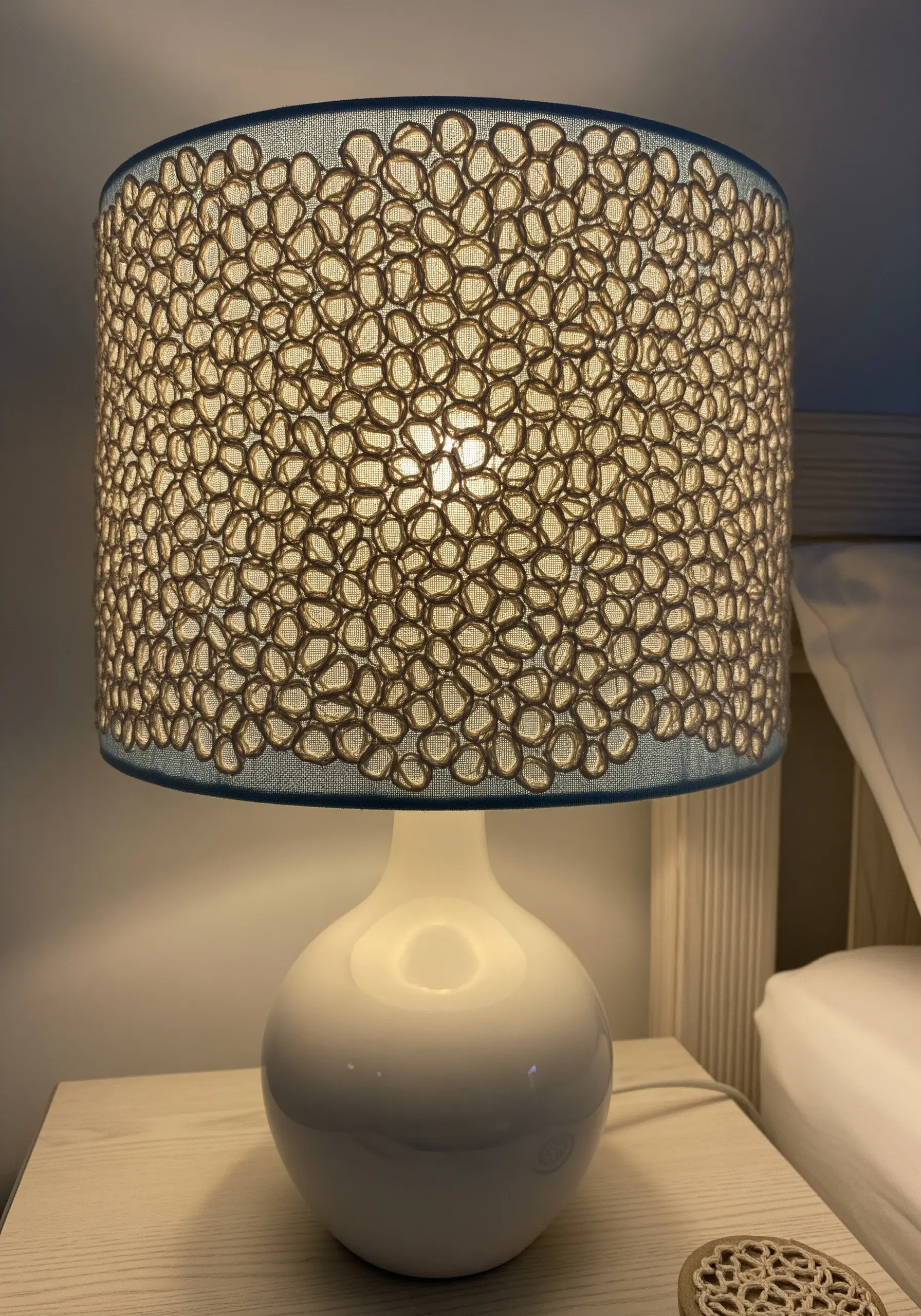 A lampshade decorated with an open-work embroidery pattern that allows light to filter through.