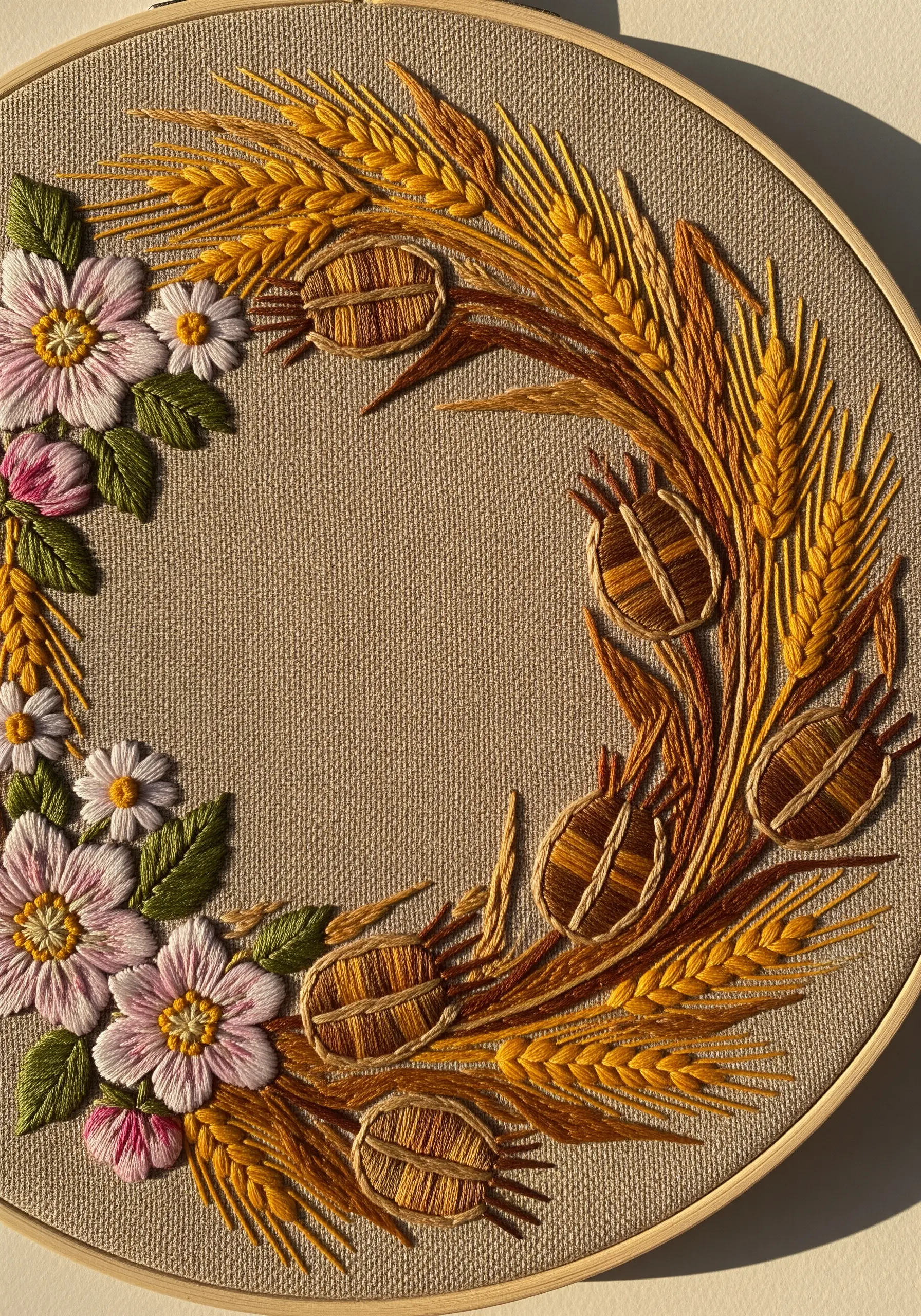 A rustic harvest wreath with embroidered wheat stalks, seed pods, and pink wildflowers.