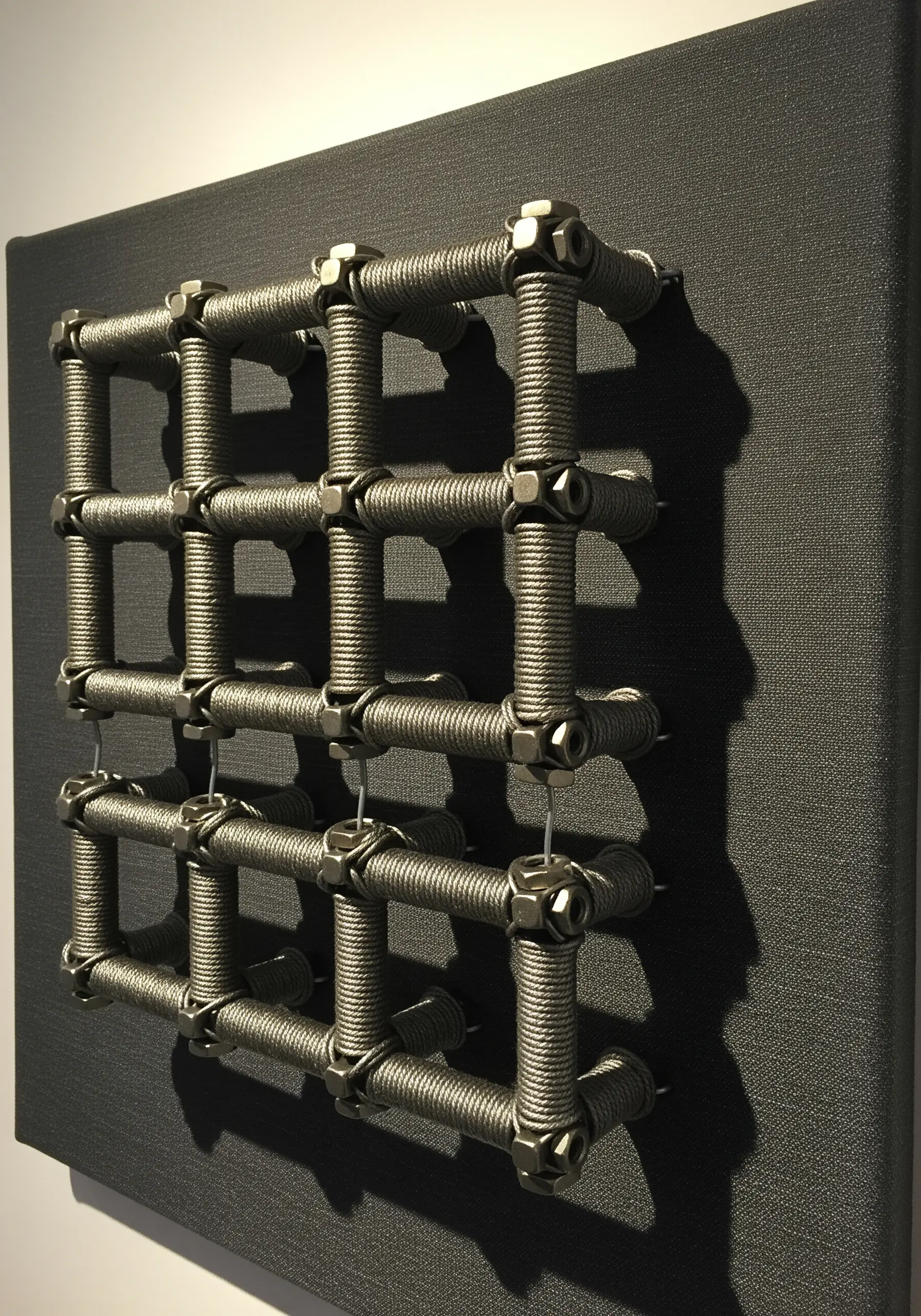 An industrial grid made of wrapped nuts and bolts, creating a 3D wall sculpture.