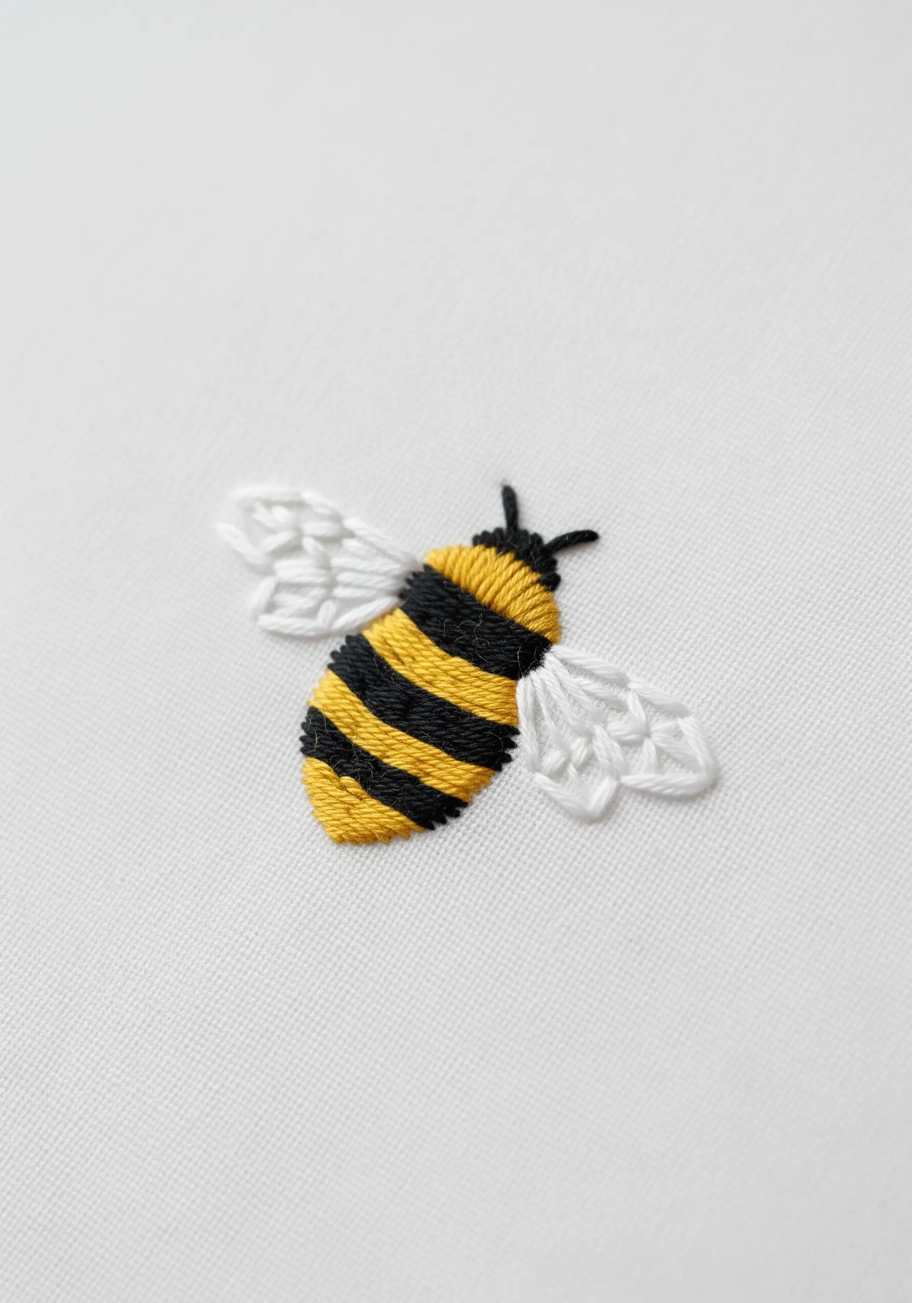 Small embroidered bumblebee with satin stitch body and fishbone stitch wings.