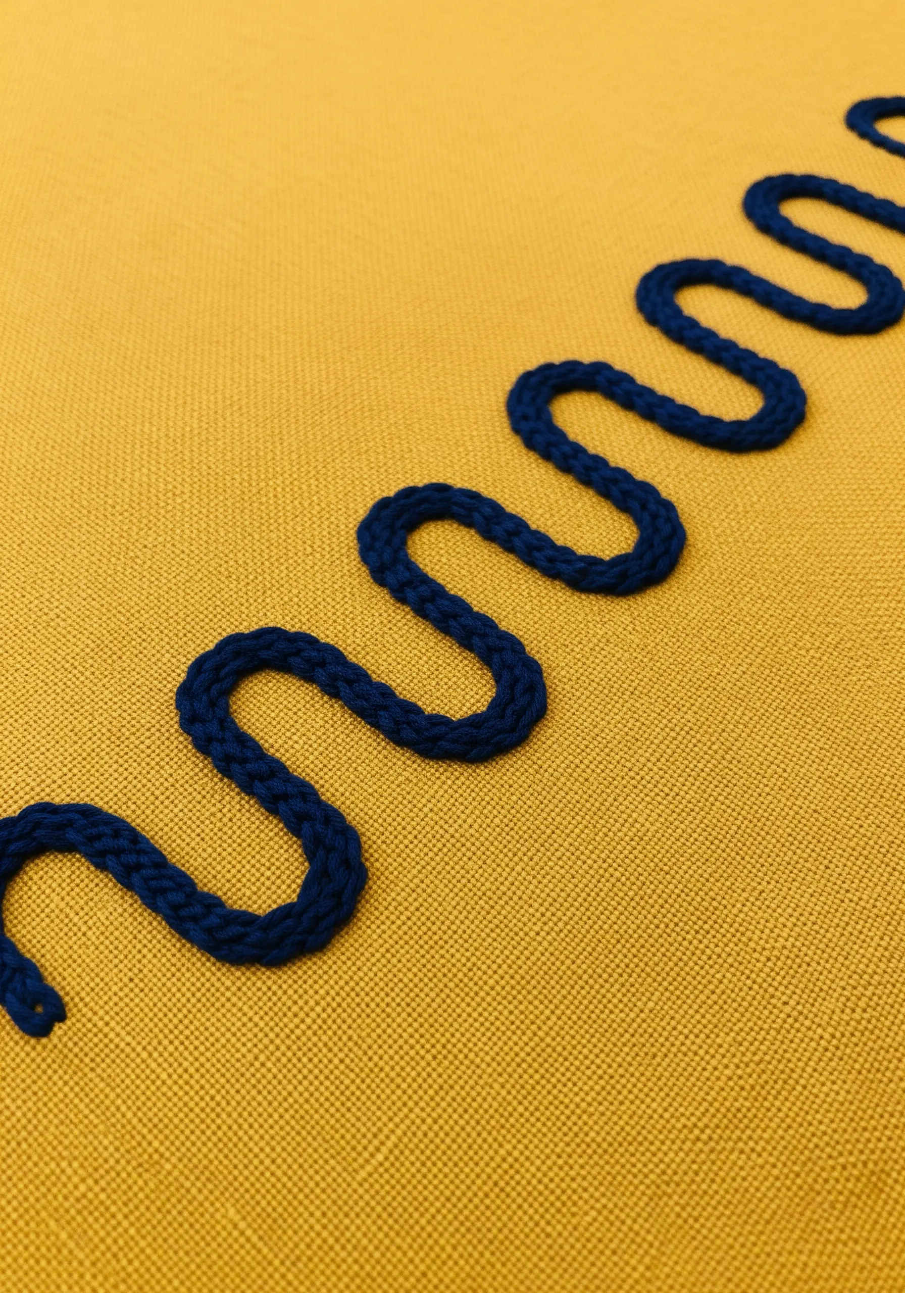 A single, thick, dark blue wavy line made with a whipped chain stitch on yellow fabric.