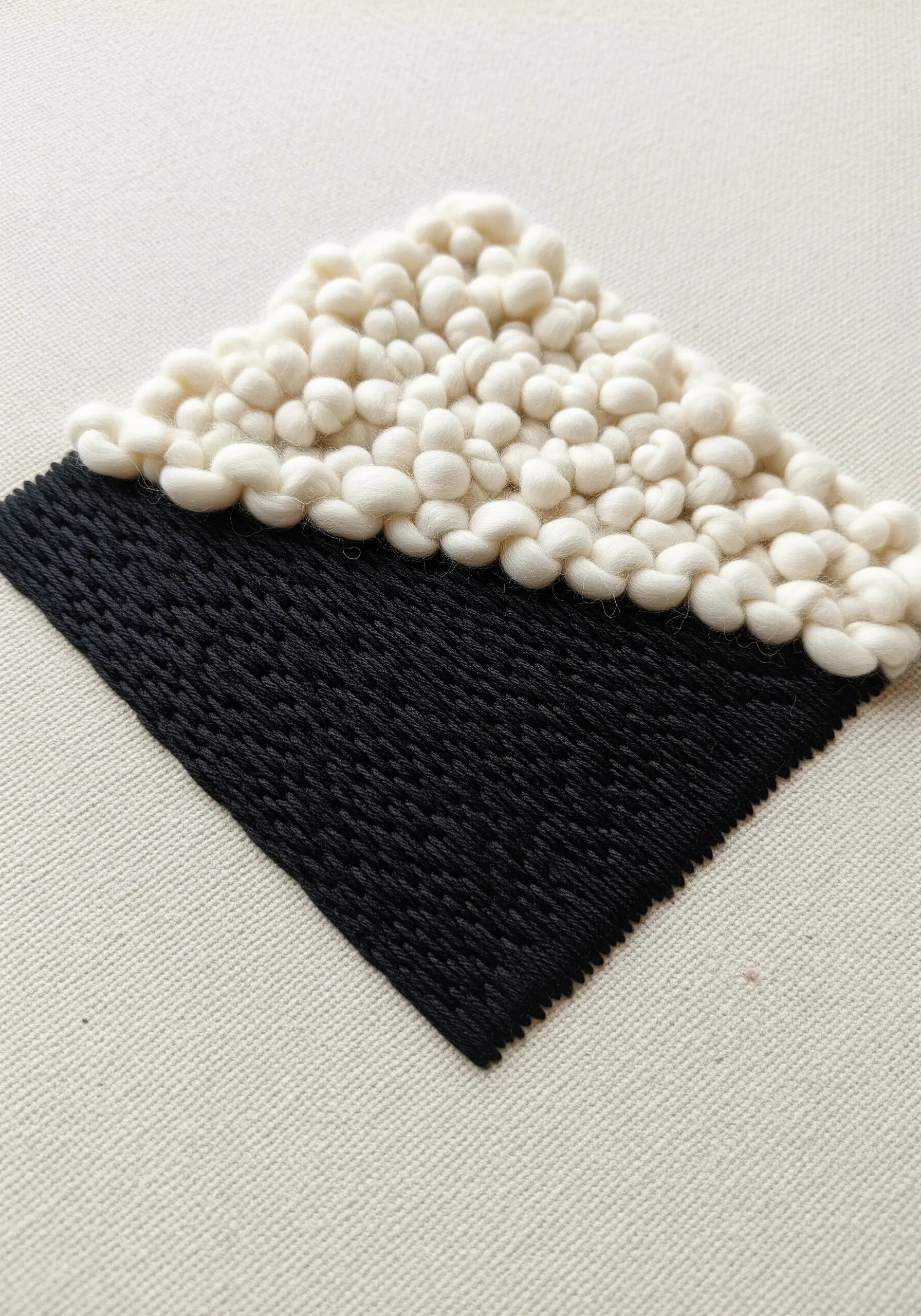 A diamond shape divided between a flat black stitch and a fluffy white wool texture.