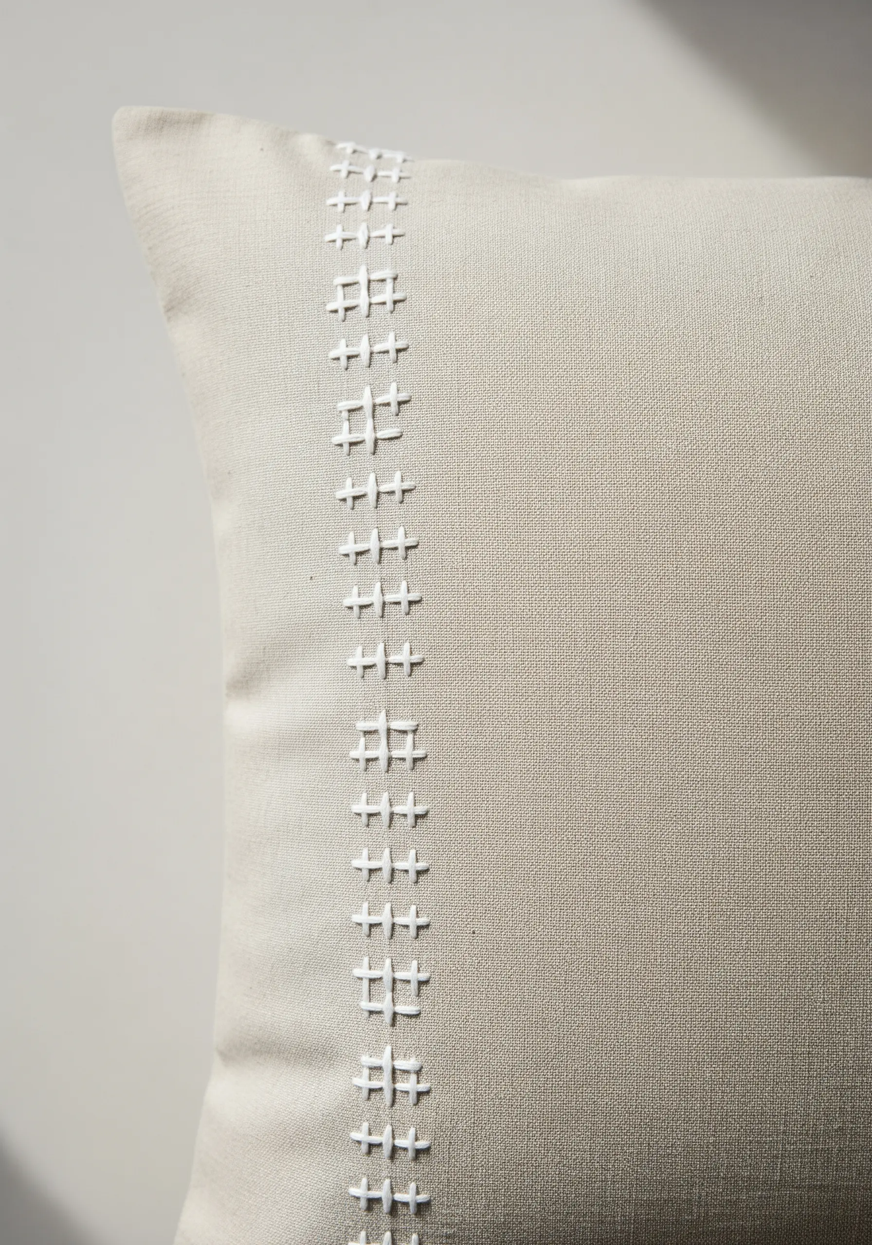 A modern geometric border in white thread on a natural linen pillow cover.
