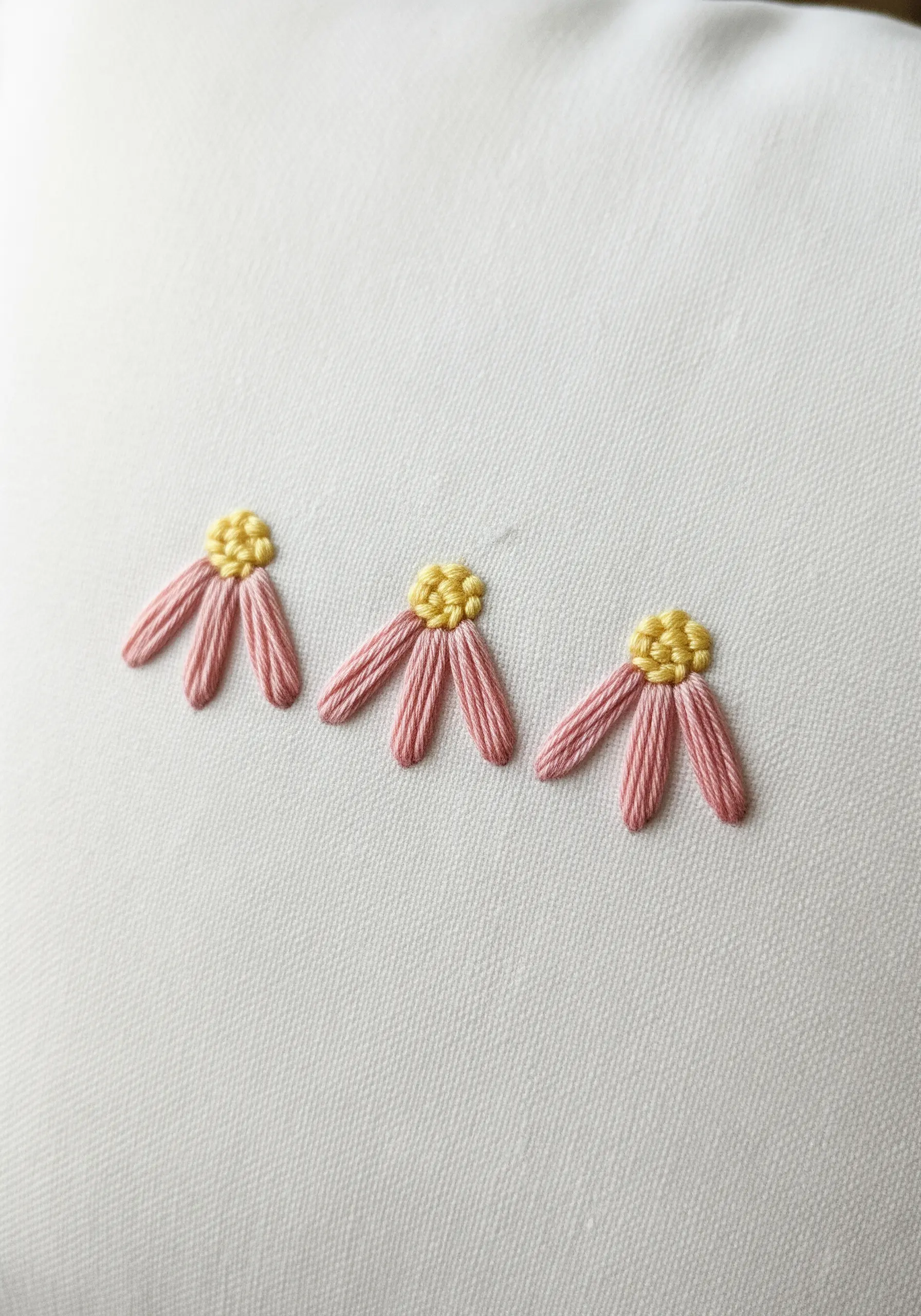 Three small pink flowers made with lazy daisy stitches and yellow French knot centers.