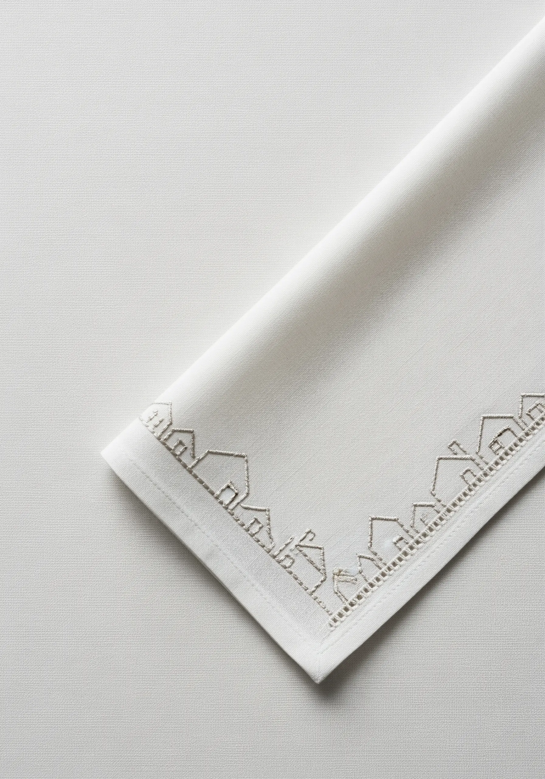 A delicate border of tiny houses embroidered in grey thread on a white napkin.