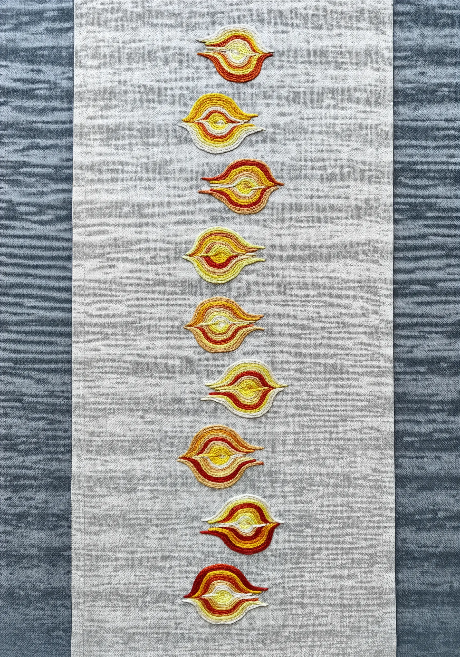 Abstract flame motifs embroidered with variegated yellow, orange, and red thread on a runner.
