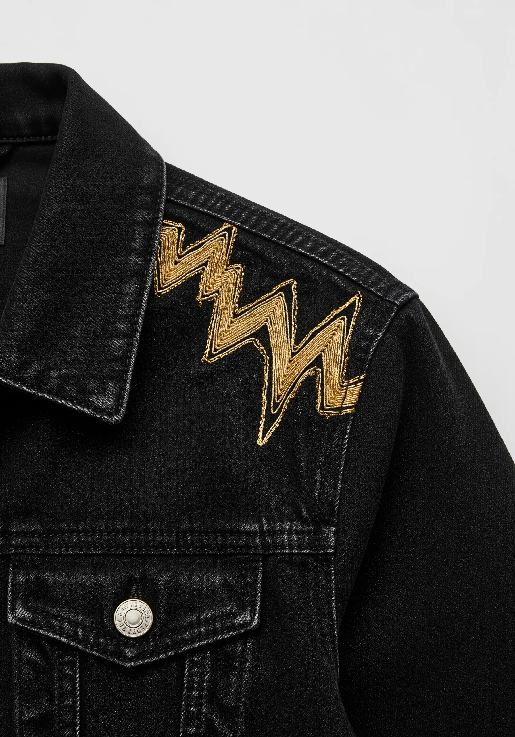 Abstract gold metallic zigzag embroidered on the shoulder of a black denim jacket.